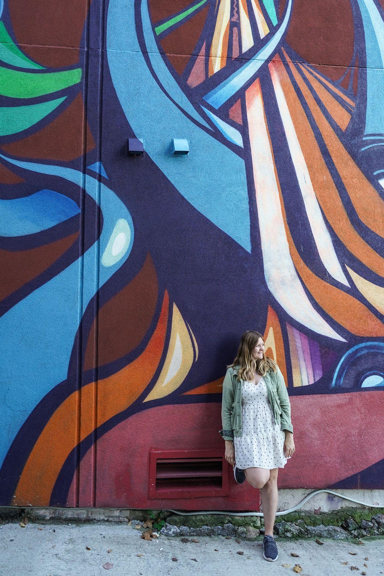 Lydia leaning against a colorful mural at the Punto Urban Art Museum