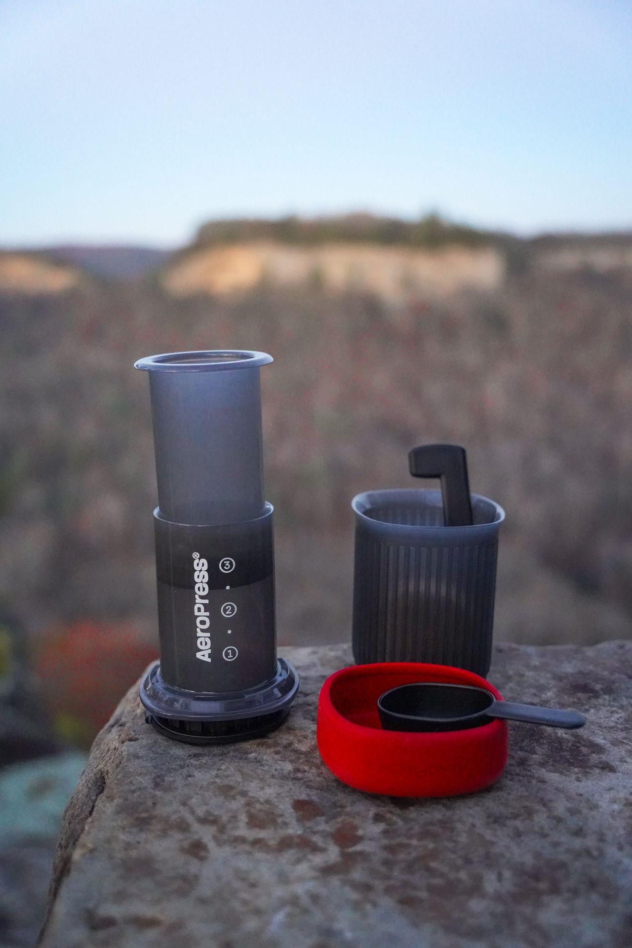An Aeropress next to a scoop sitting outside.