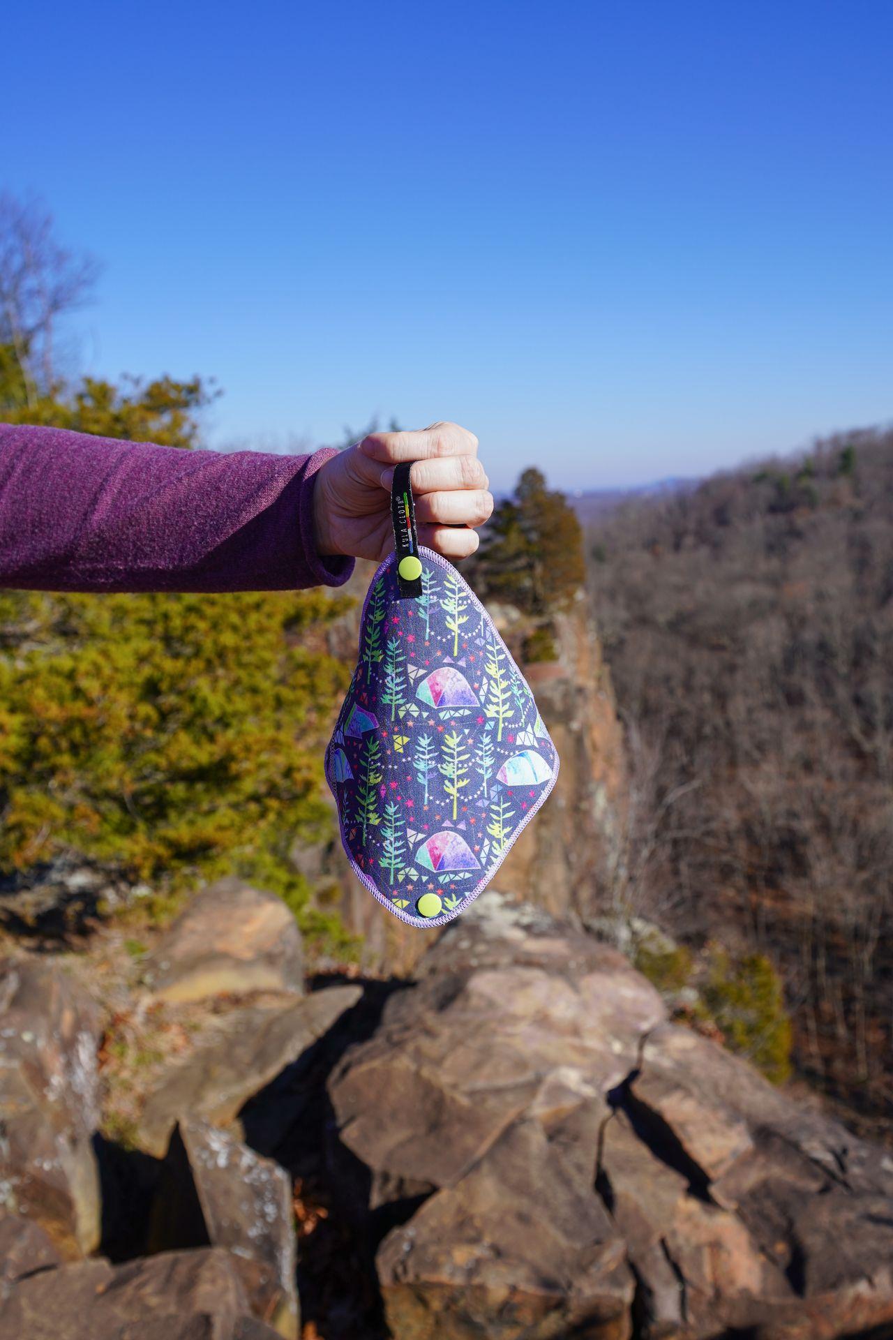 Holding up a Kula Cloth that features a design with tents and trees.