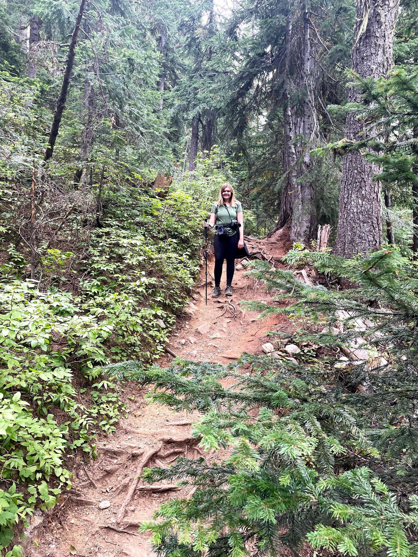 Lydia facing the camera up on a hill during a hike in Washington. She has a trekking poll and her jacket tied around her waist.