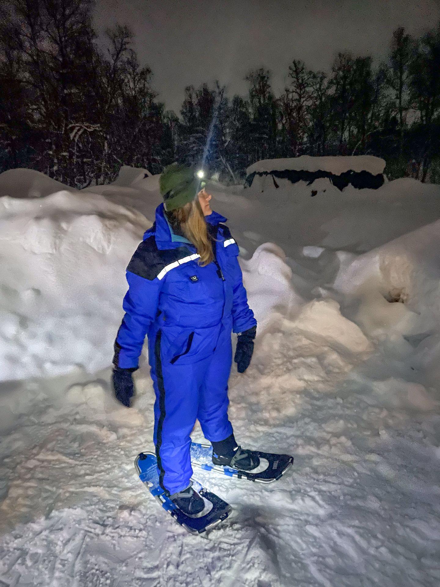 Lydia wearing a blue snowsuit and snowshoeing in the dark at the Tromso Ice Domes