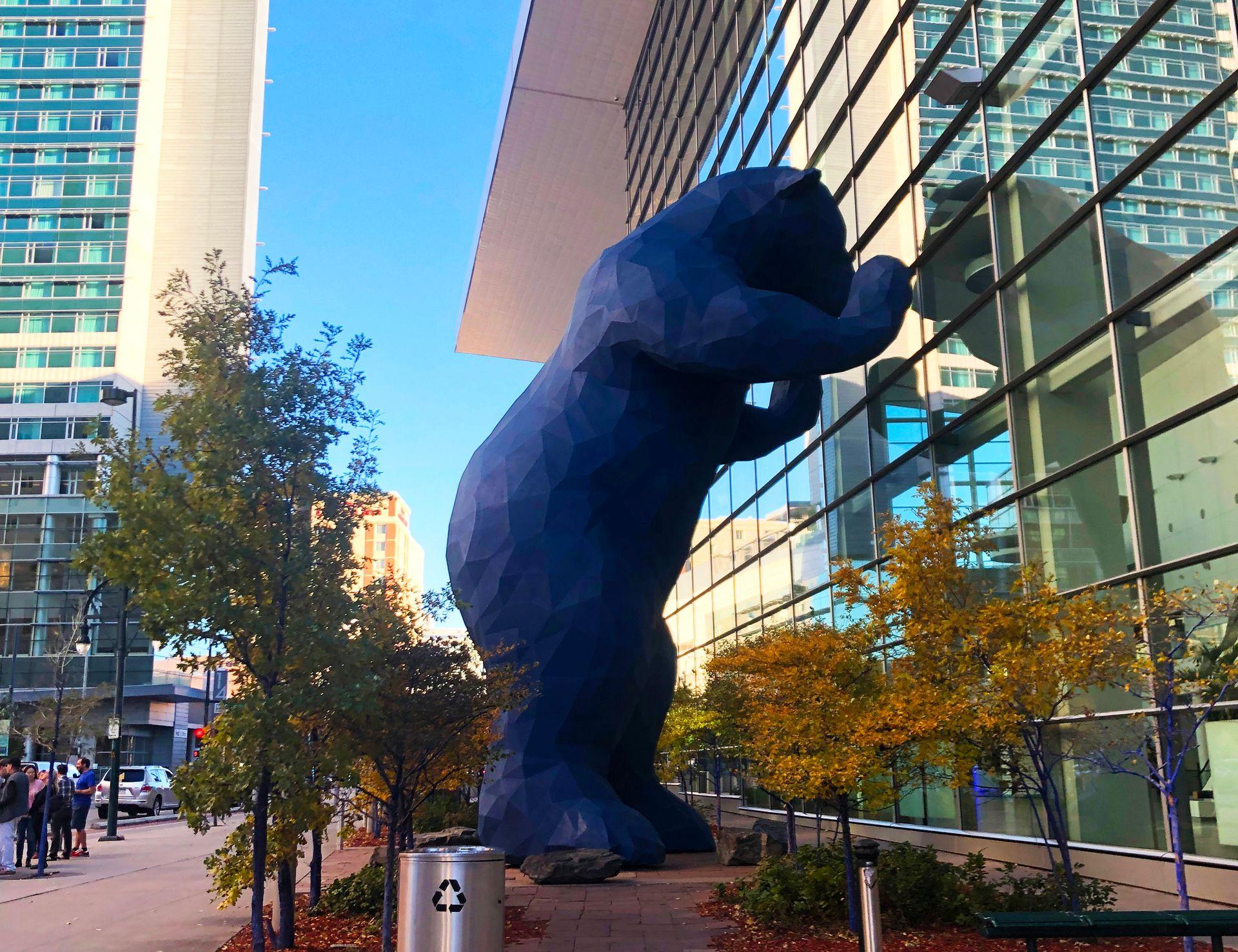 A giant blue bear leading up against a glass window outside of the Denver Convention Center.