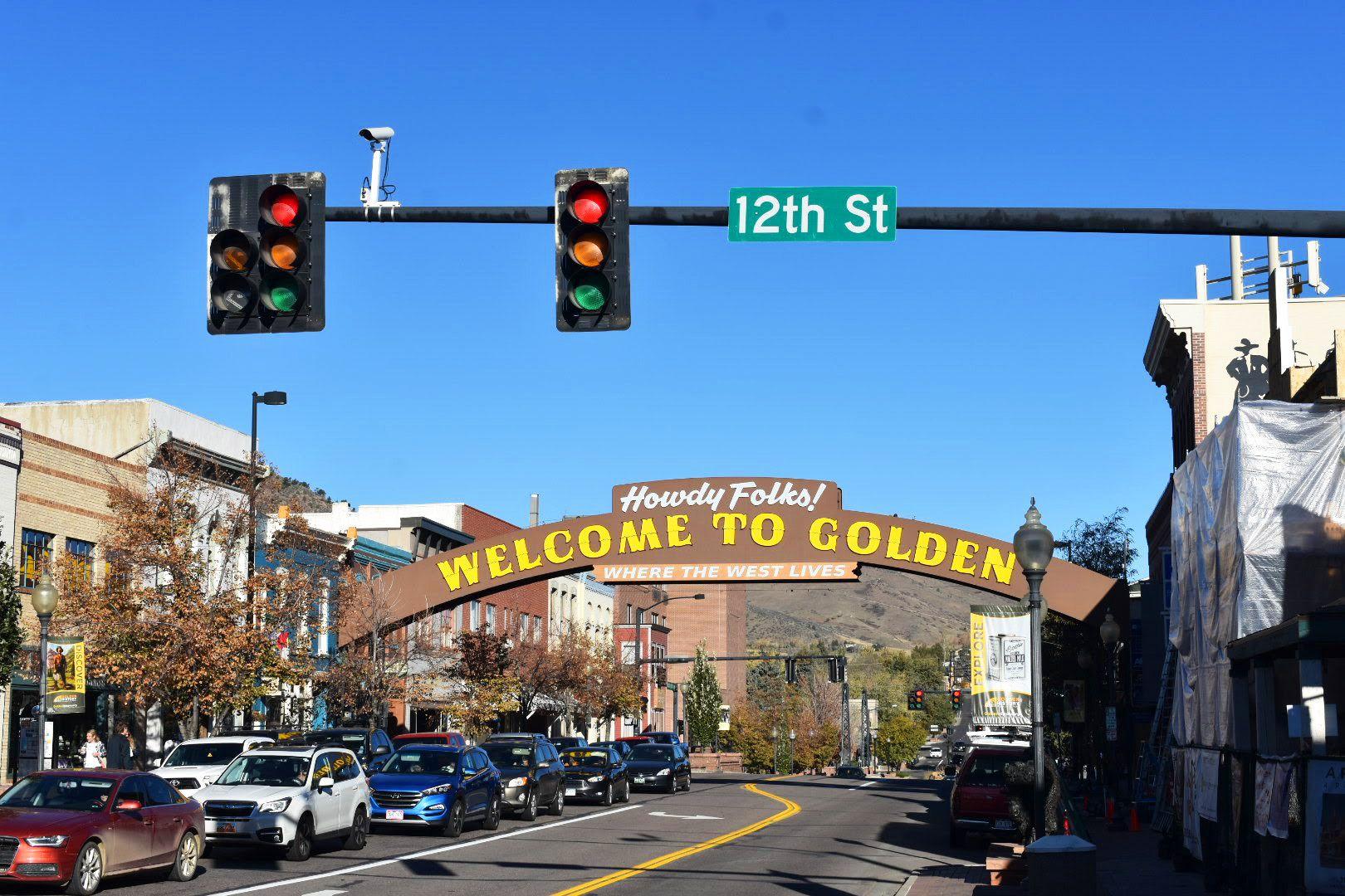 A street in Golden, CO. A large arch extends over the road and reads "Howdy Folks, Welcome to Golden"