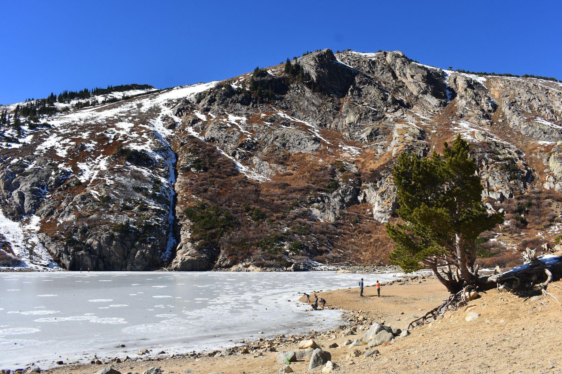 A view standing next to the frozen St. Mary's Lake. There is a mountain in the background and a tree next to the water.