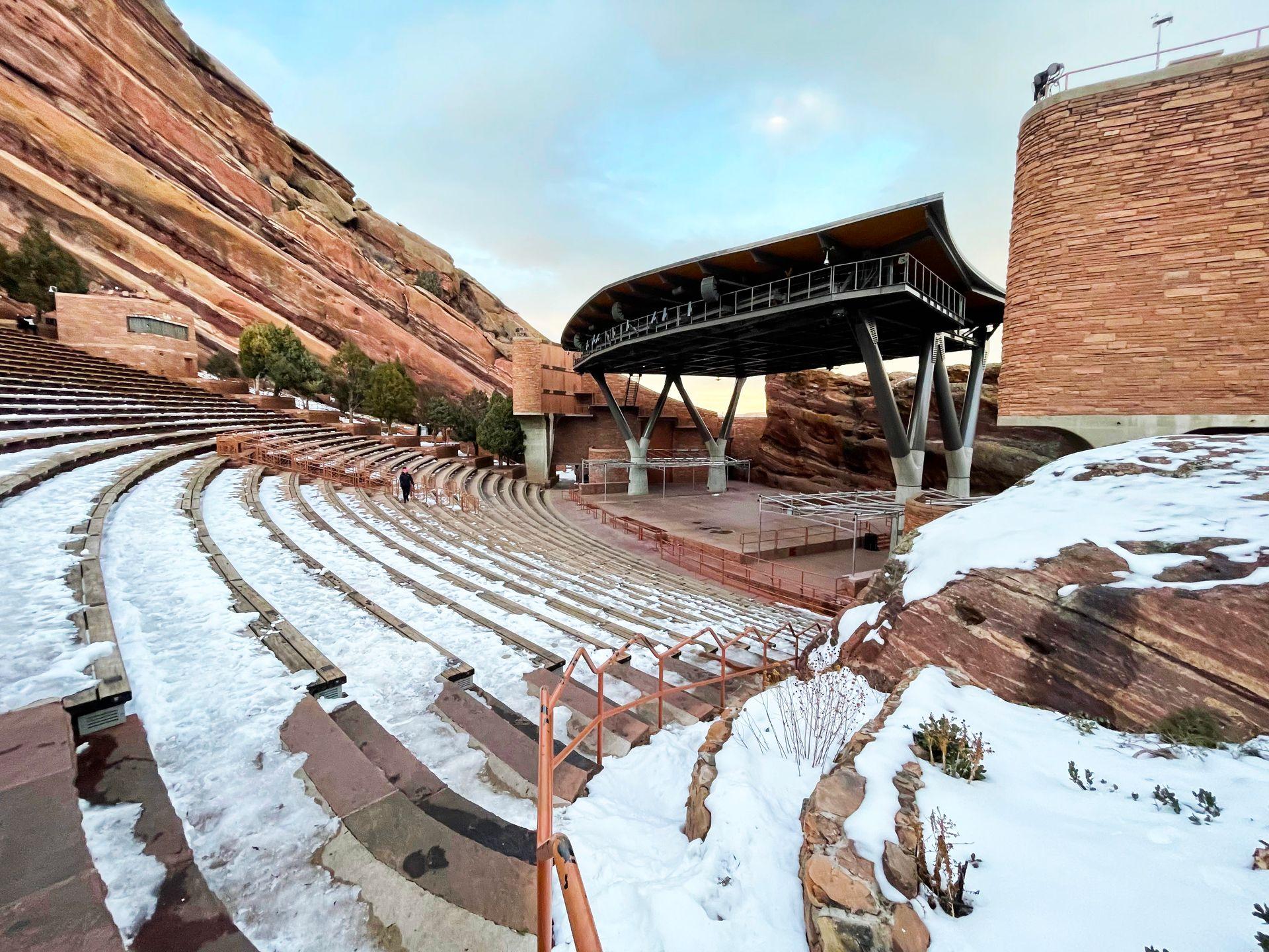 Red Rock Ampitheatre covered in snow. Snow is one the bleachers and the stage is surrounded by huge orange rocks.