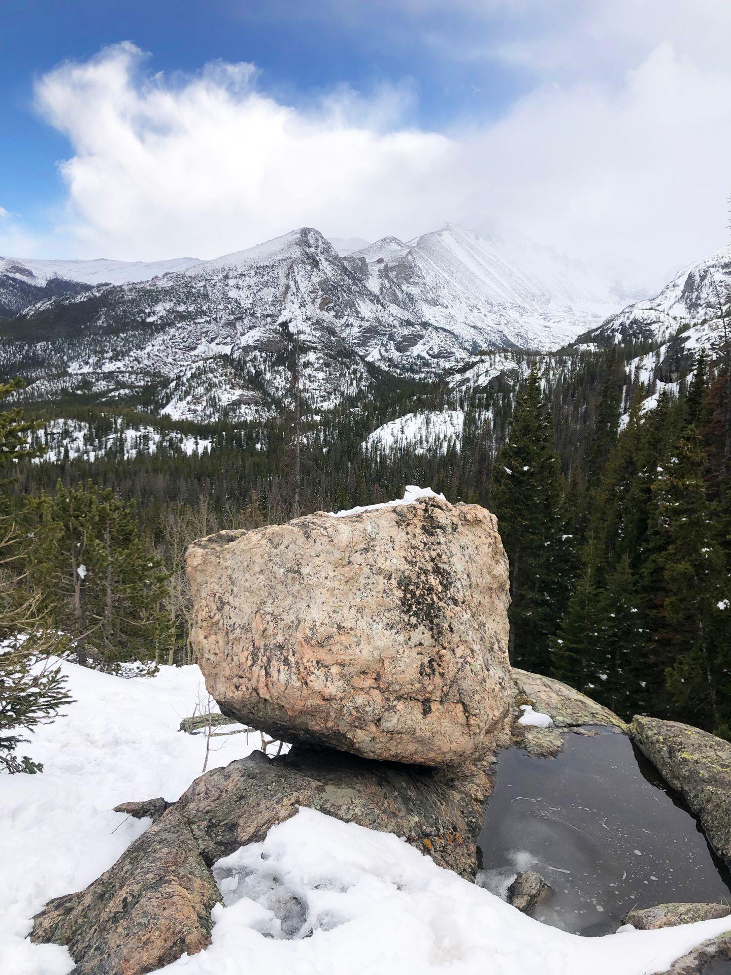 A pile of boulders covered in some snow with snowy mountains in the distance.
