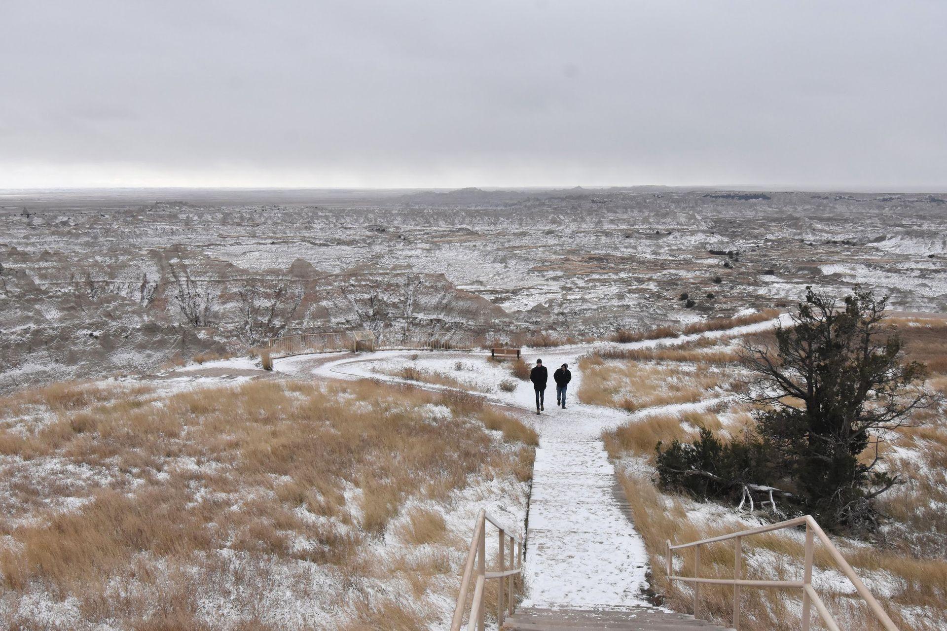 Two people walking on a snowy trail in the Badlands.