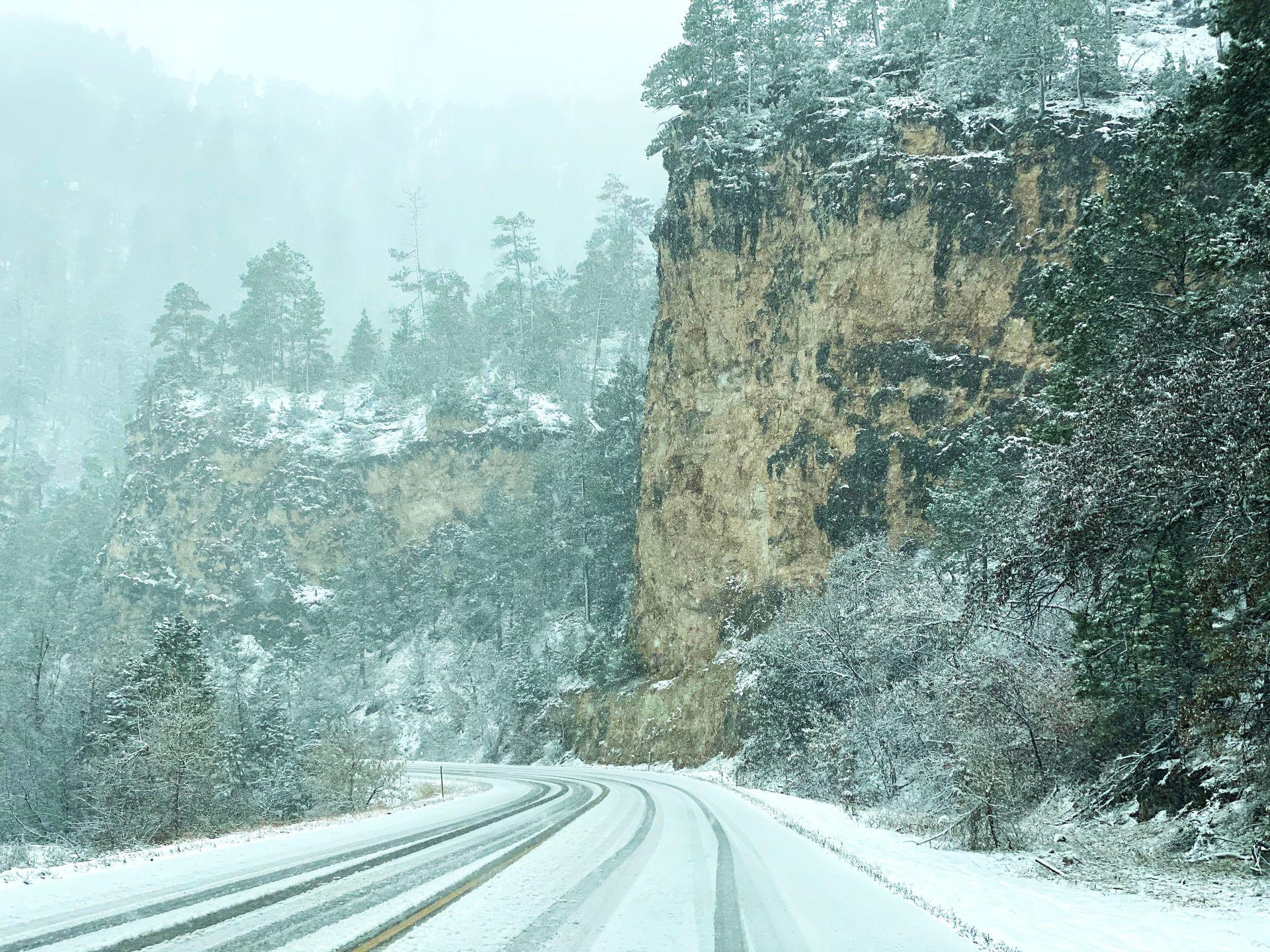 A snow covered road with a rock towering up on one side.