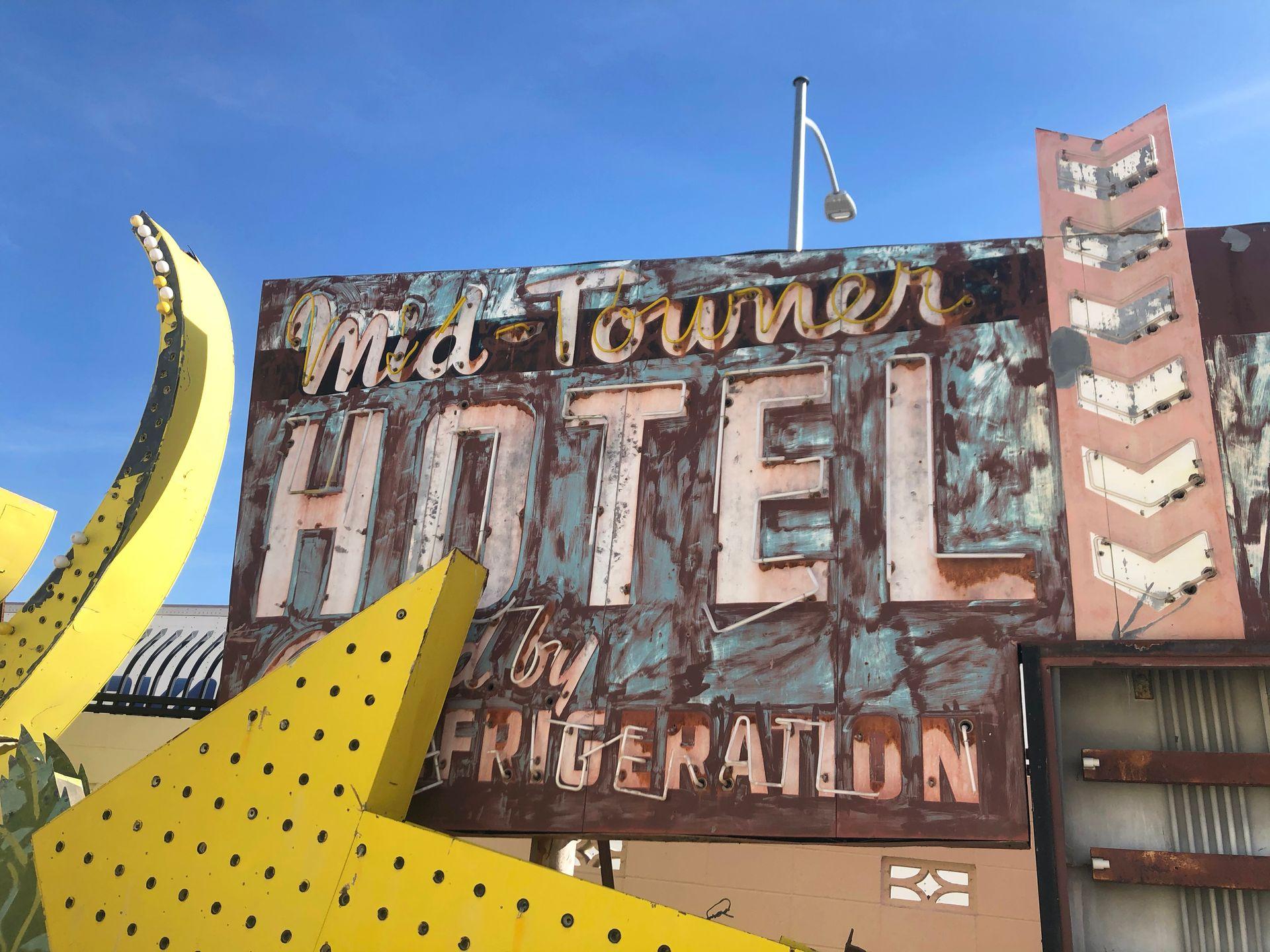 A pink hotel sign and a giant yellow arrow at the Neon Museum.
