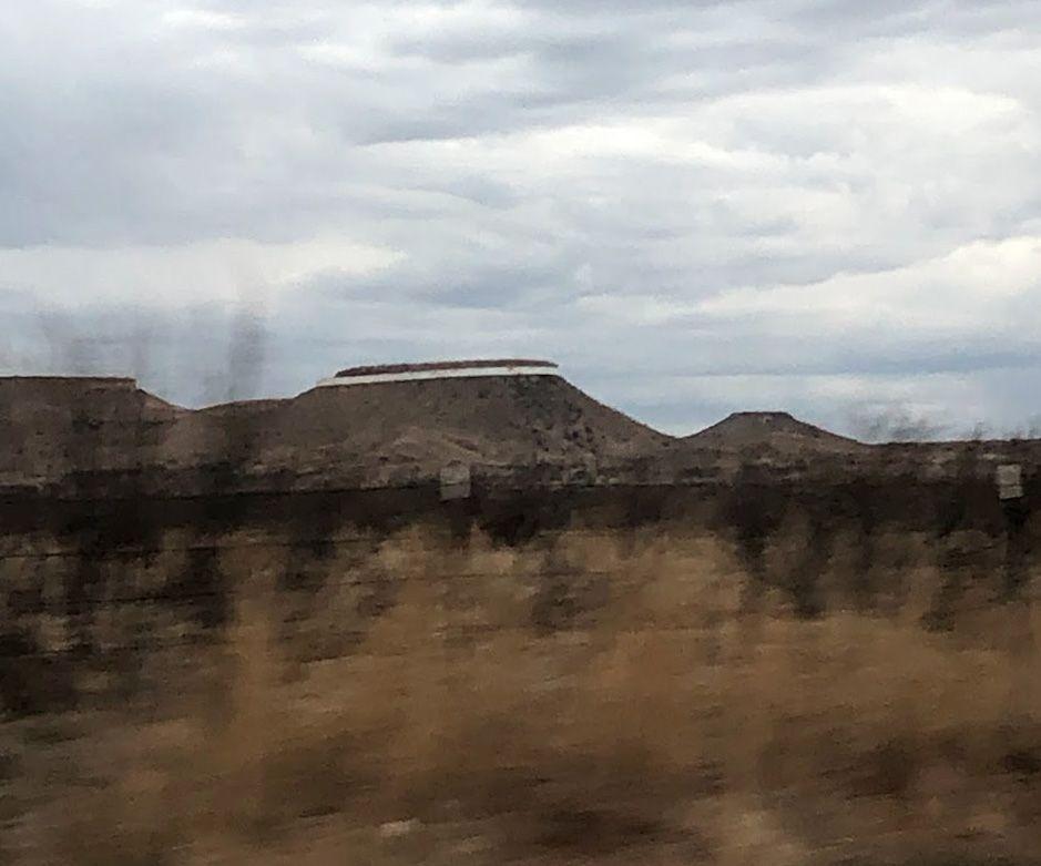 A blurred photo of a mesa with a reflective strip near the top. Taken while driving by.