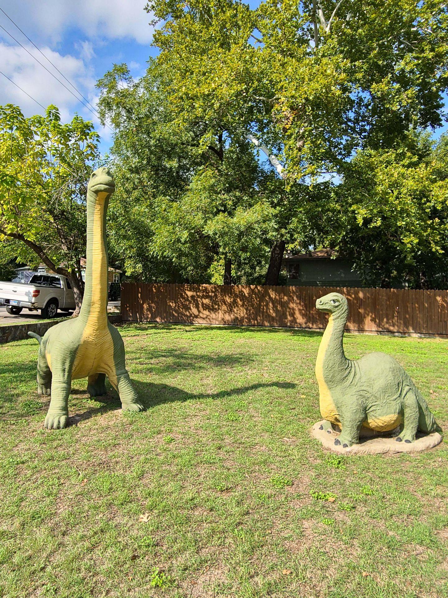 Two green dinosaur statues in the grass in downtown Glen Rose.