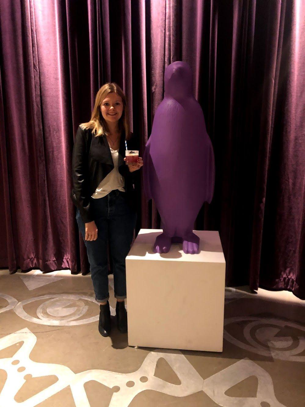 Lydia standing next to a purple penguin holding a cocktail.