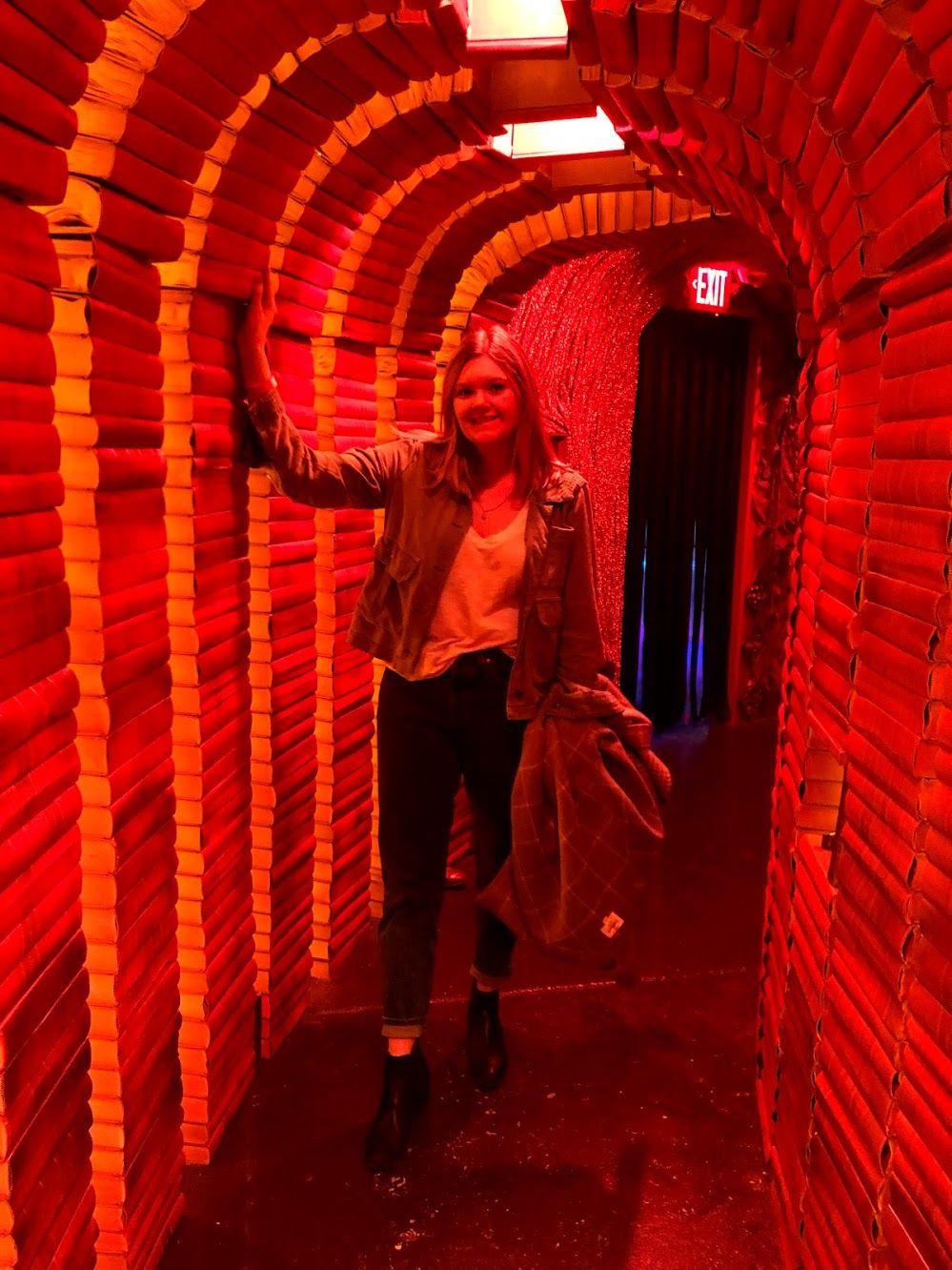Lydia standing in a red tunnel made out of books.