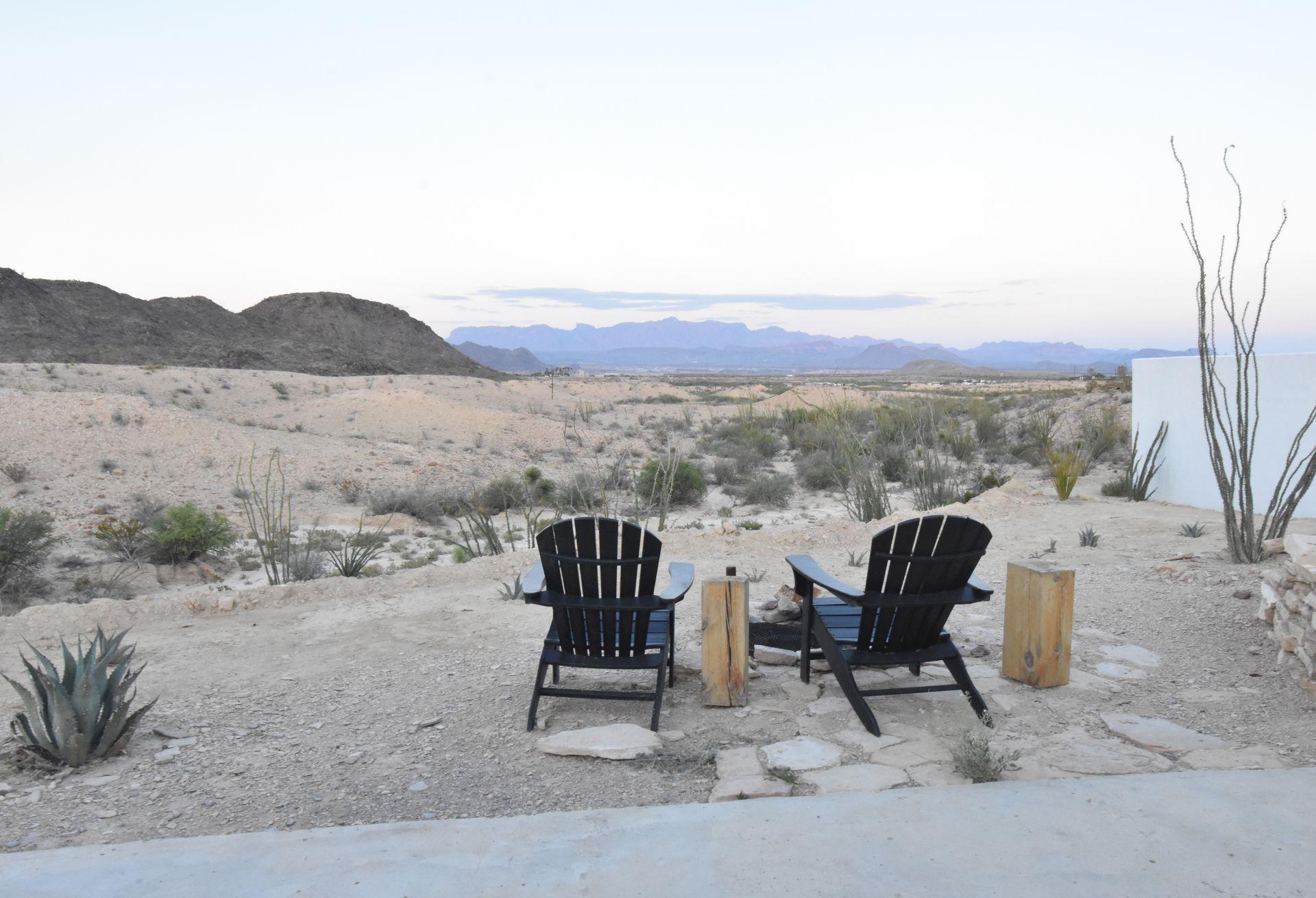 Two black lounge chairs in front a firepit with desert views in front of them.