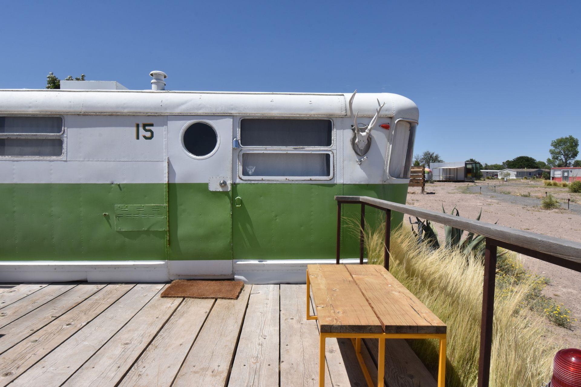 The exterior view of a green and white trailer with a deck in front of it.