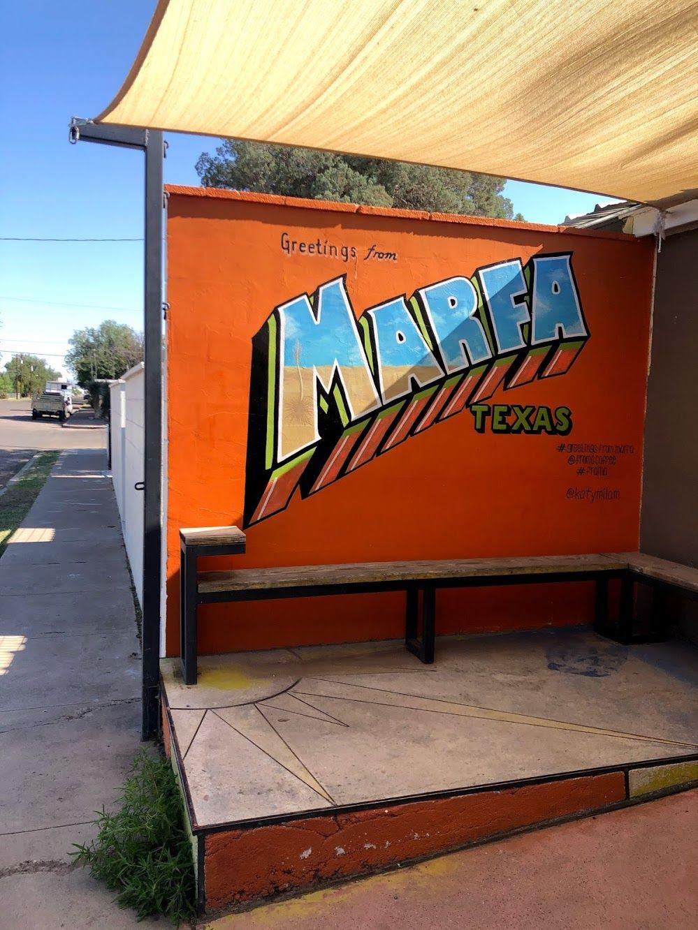 A 'Greetings from Marfa' mural on a orange walls outside of Frama Coffee