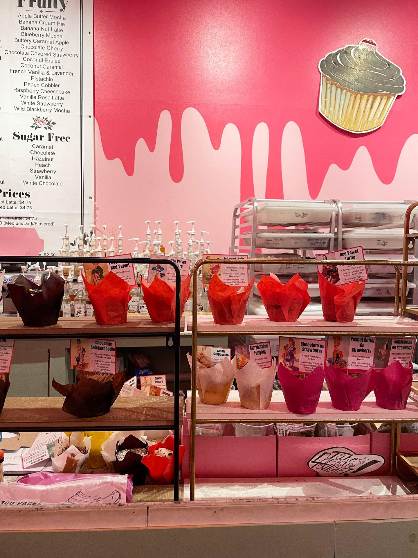 Some shelves sit on a counter with several cupcakes on them. The cupcakes are wrapped in red, white and purple paper.