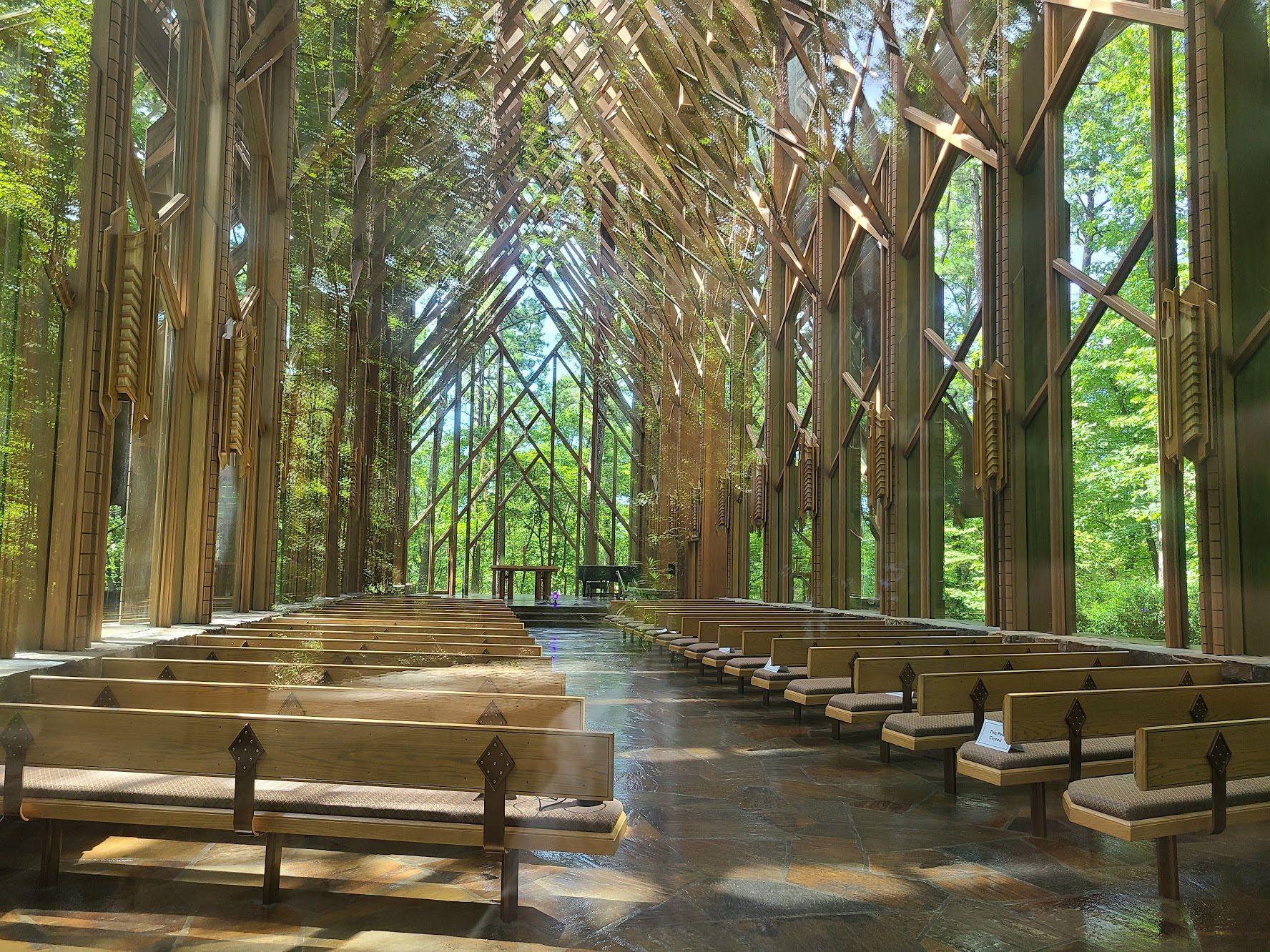 The inside of Anthony Chapel. There are bench seats and you can see the surrounding forest through all of the glass.