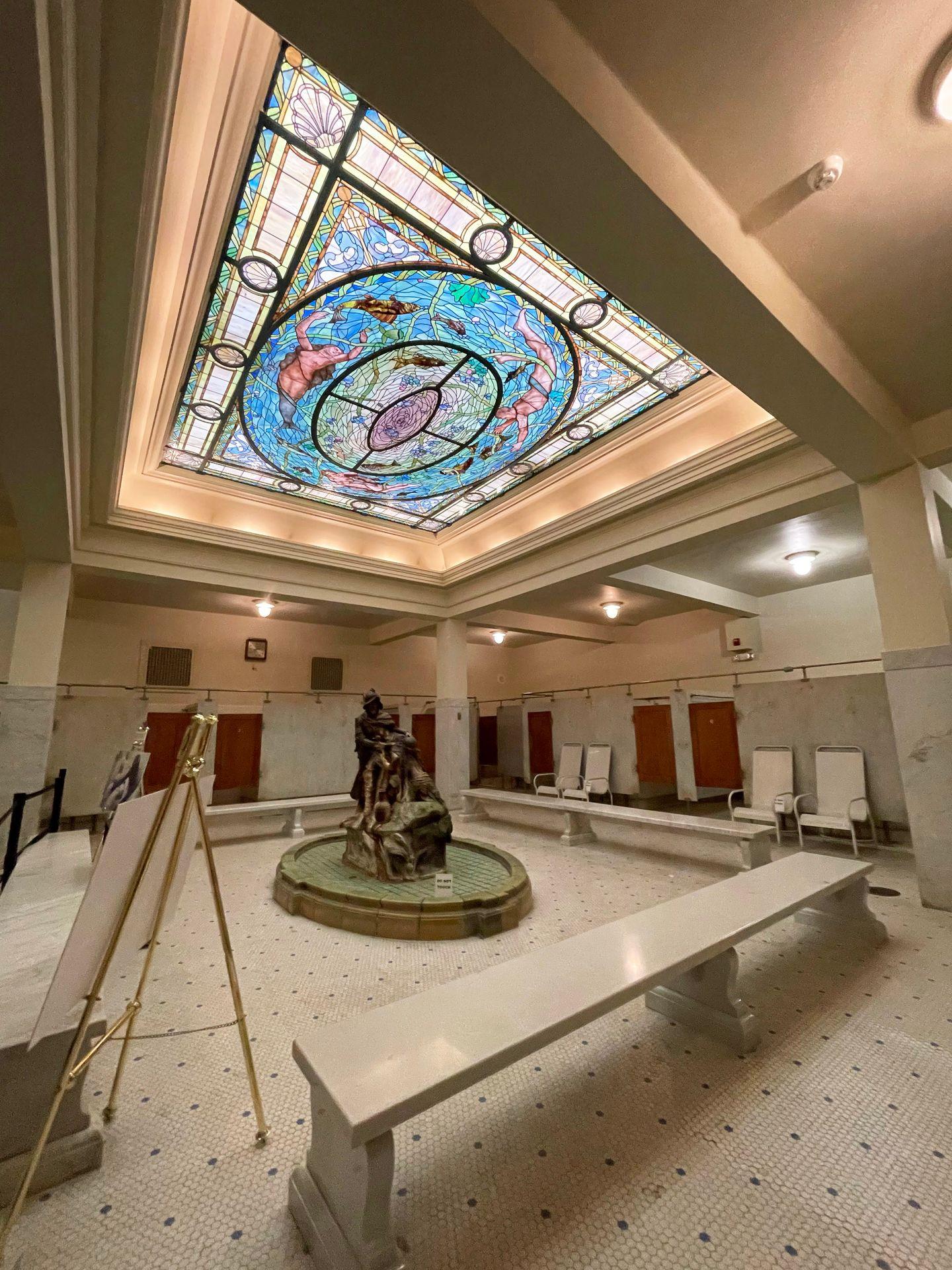The former locker rooms of the Fordyce Bathhouse. There is an orante stained glass ceiling and a statue in the center of the room.