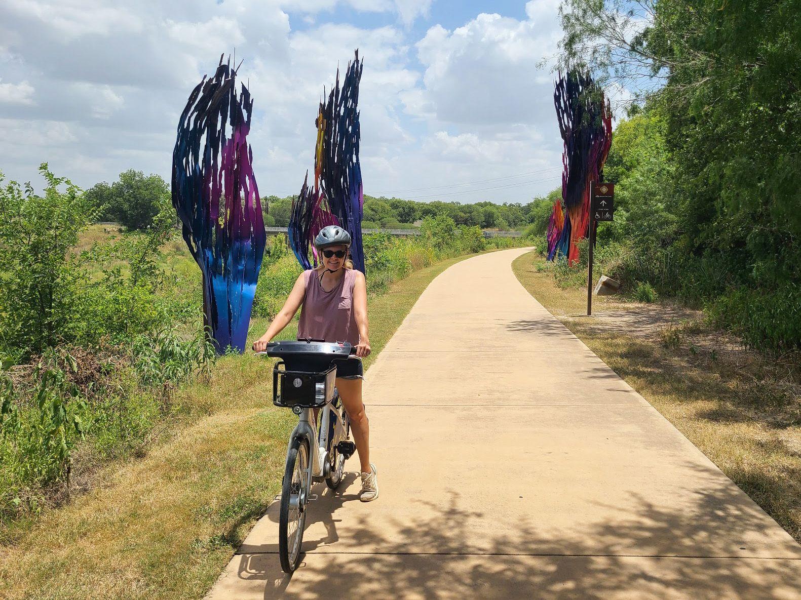 Lydia riding a bike on a paved path with a colorful sculpture behind her on each side of the trail.