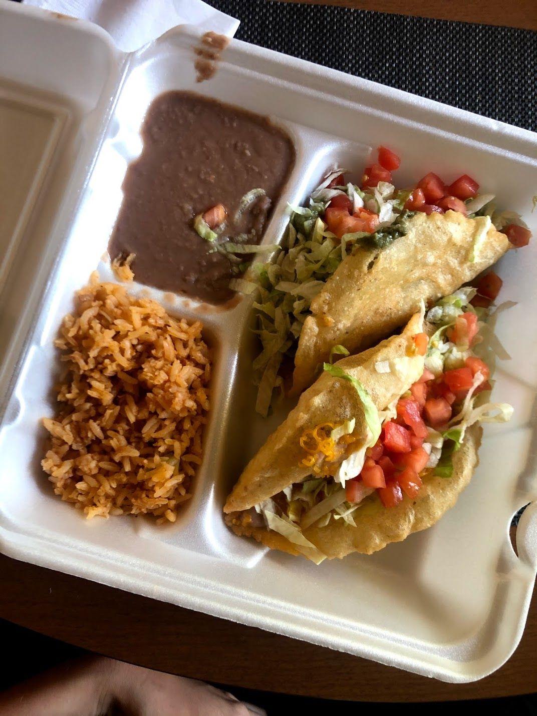 A take out box with tacos, refried beans and rice. The taco shells look like puffy tortilla chips.