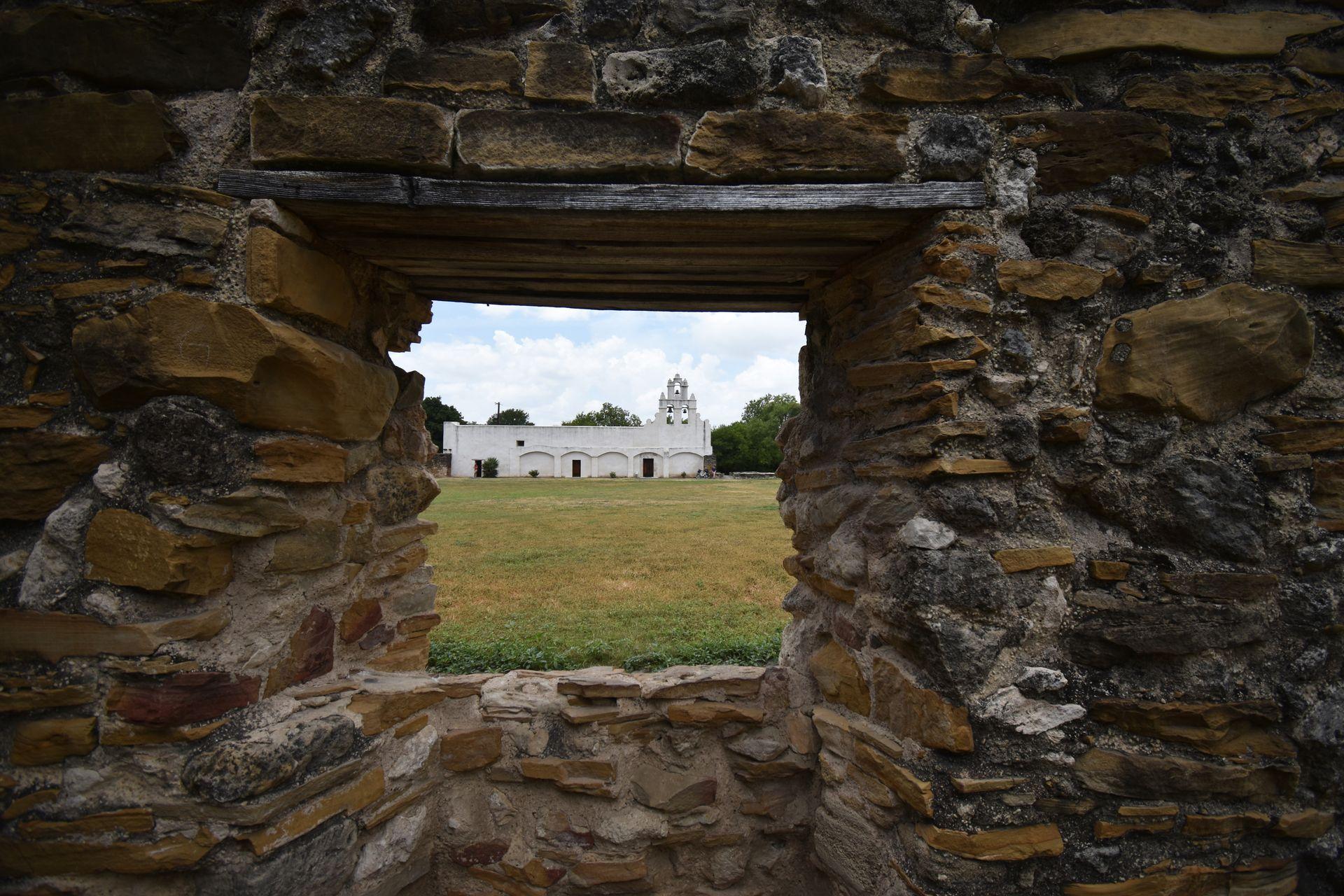 Looking through a square, brick window to see the white Mission San Juan in the distance.