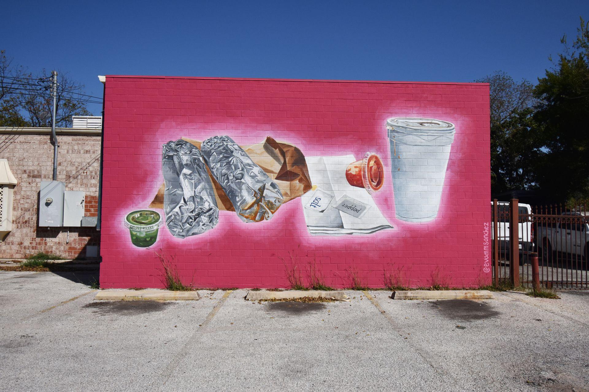 A pink mural with foil wrapped tacos, green and red salsa containers and a cup.