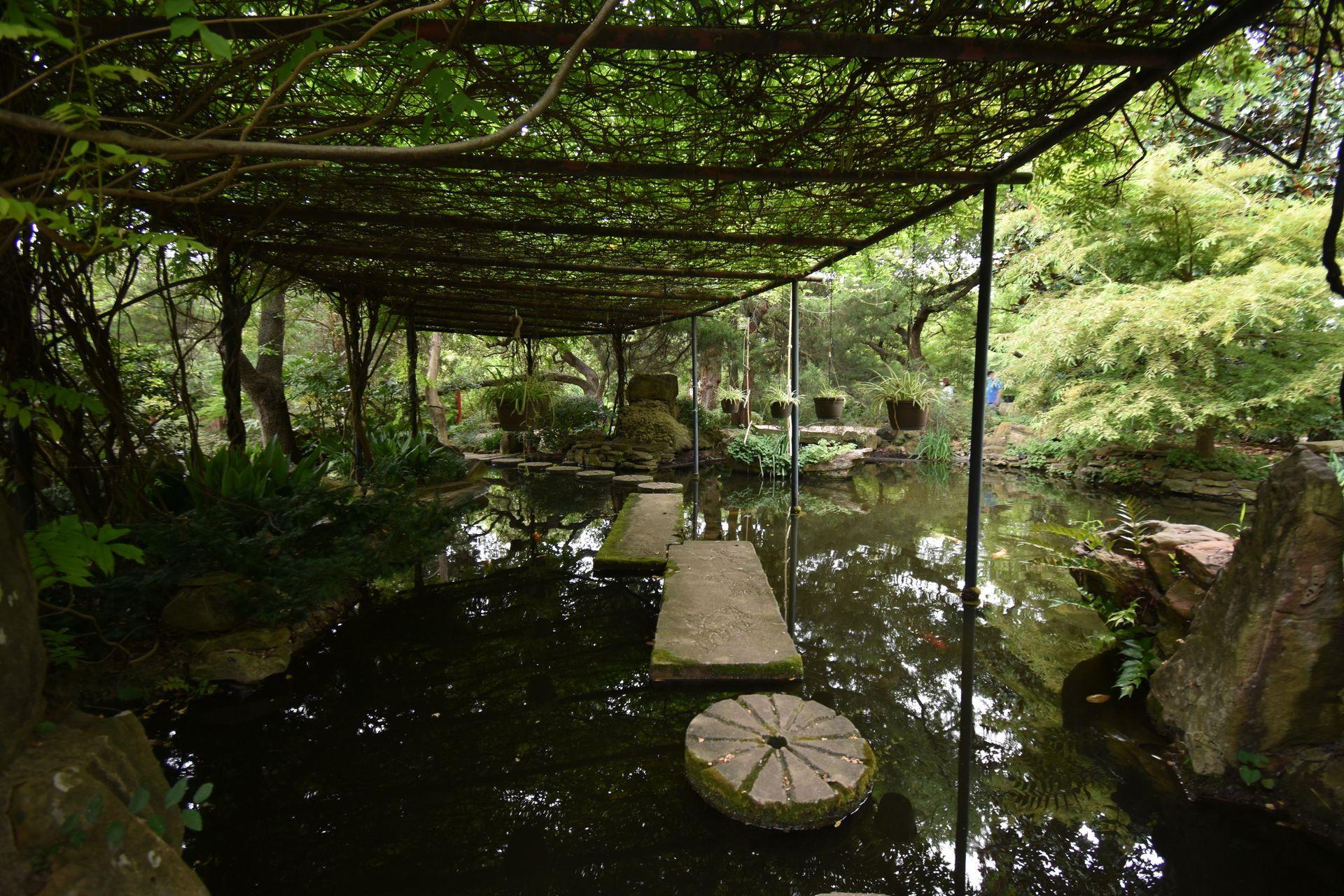 A stone pathway over water with a canopy above it at Chandor Gardens.