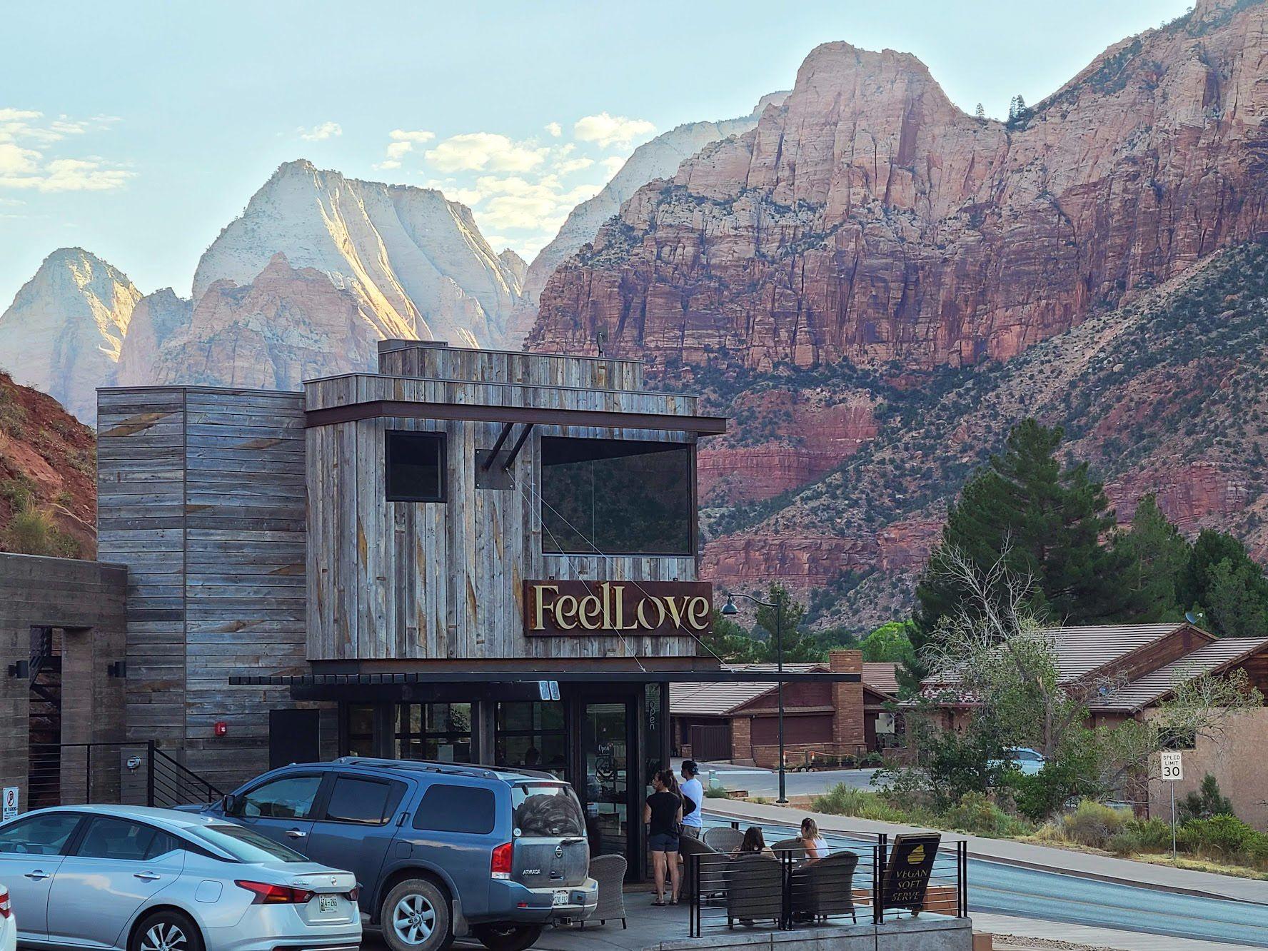 A rustic coffee shop that reads "Feel Love" with the orange cliffs of Zion in the background.