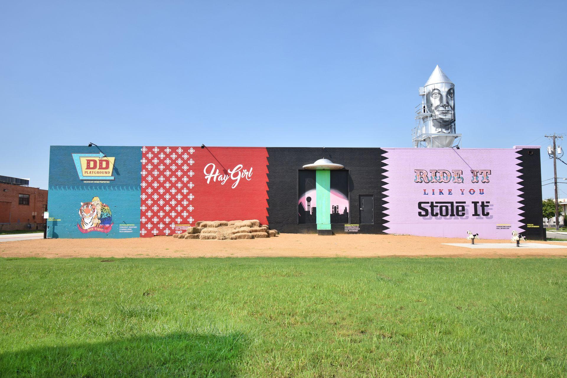 A wall of colorful murals, including one that says "Hay Girl" with hay bails below it and a pink wall that says "Ride it like you Stole It" with pony rides below it.