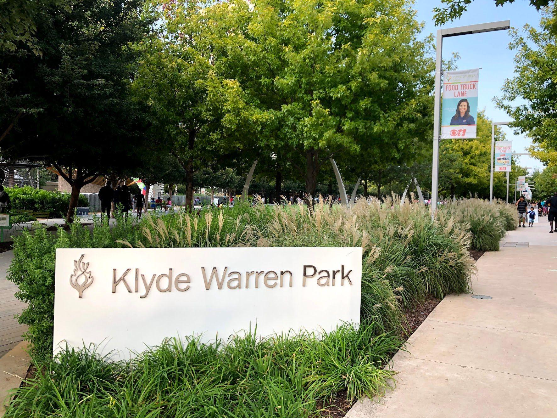 A sign of Klyde Warren Park next to a sidewalk.