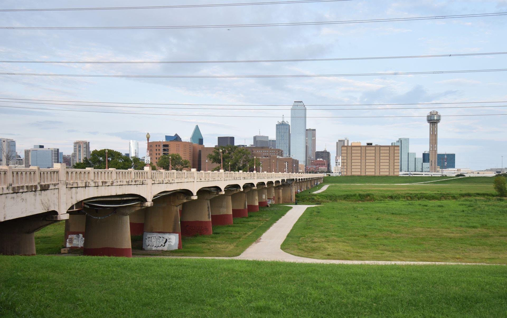A view of downtown Dallas from the Trinity Overlook Park. There is an expansive green space and a bridge before the city.