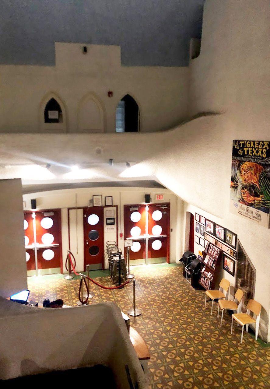 Looking down at the lobby inside the Texas Theater. There red doors with round windows, a colorful carpet and white walls.