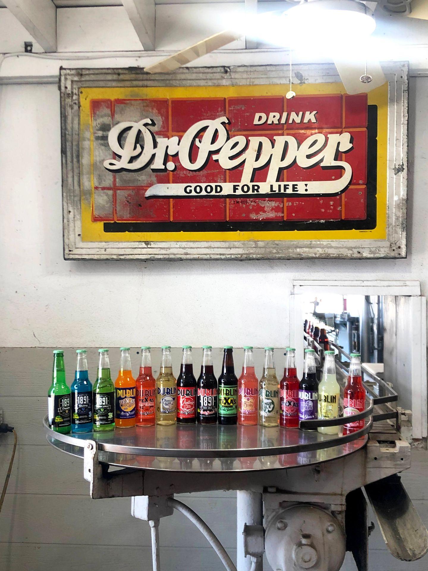 A sign reads "Drink Dr. Pepper: Good for Life" above a metal table that has all of the offerings for Dublin sodas.