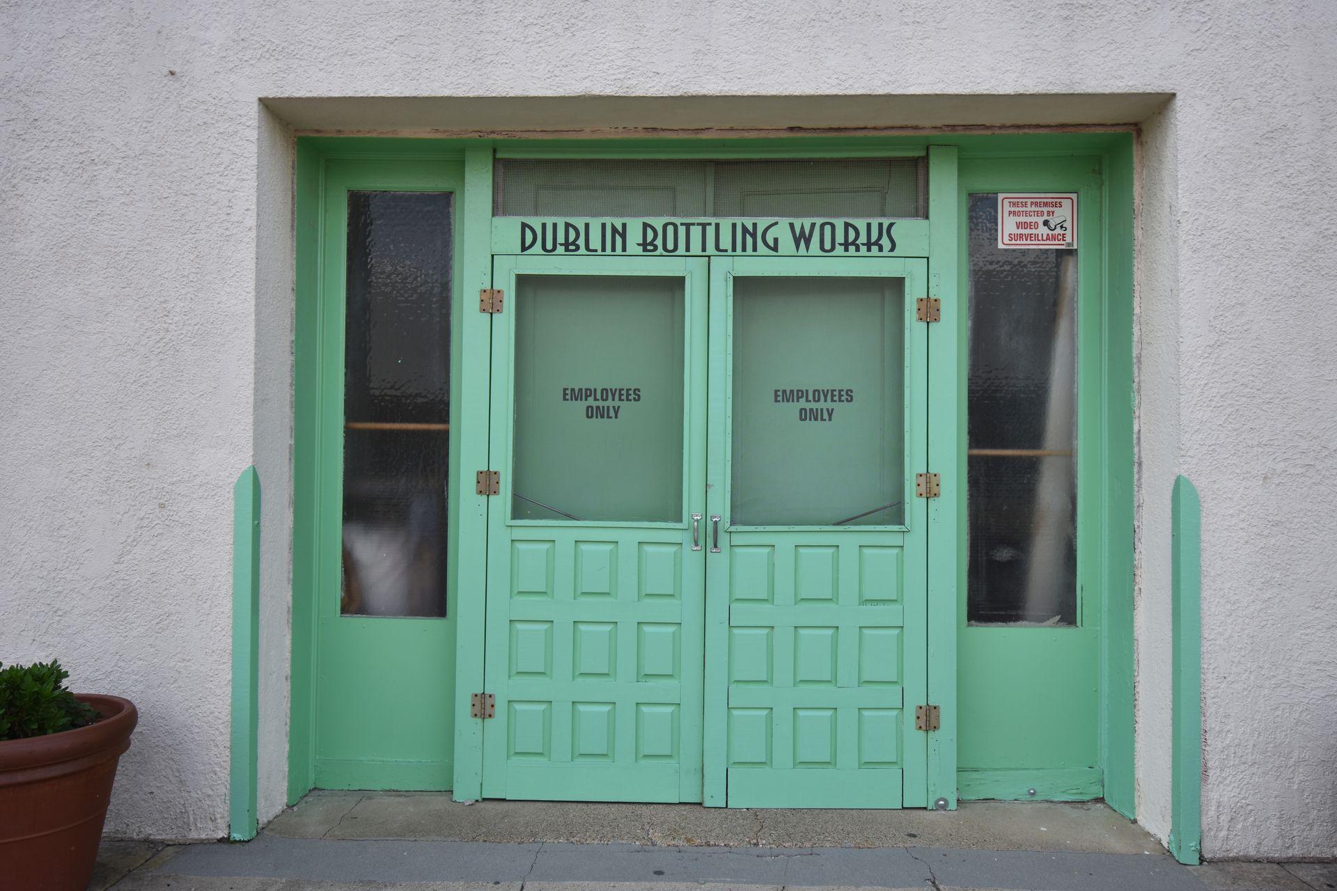 A set up green doors with the words "Dublin Bottling Works" above them. There are signs on the doors that say Employees Only