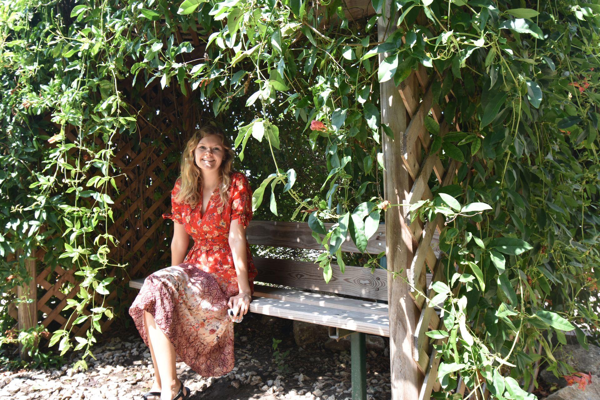 Lydia sitting on a wooden bench that is surrounded by green vines.