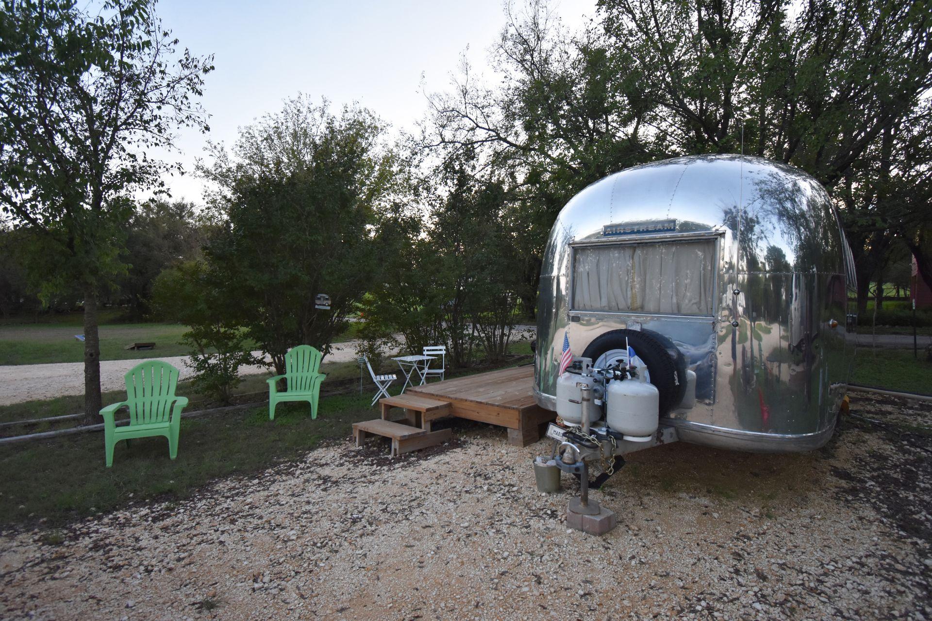 A silver airstream with some green chairs next to it.