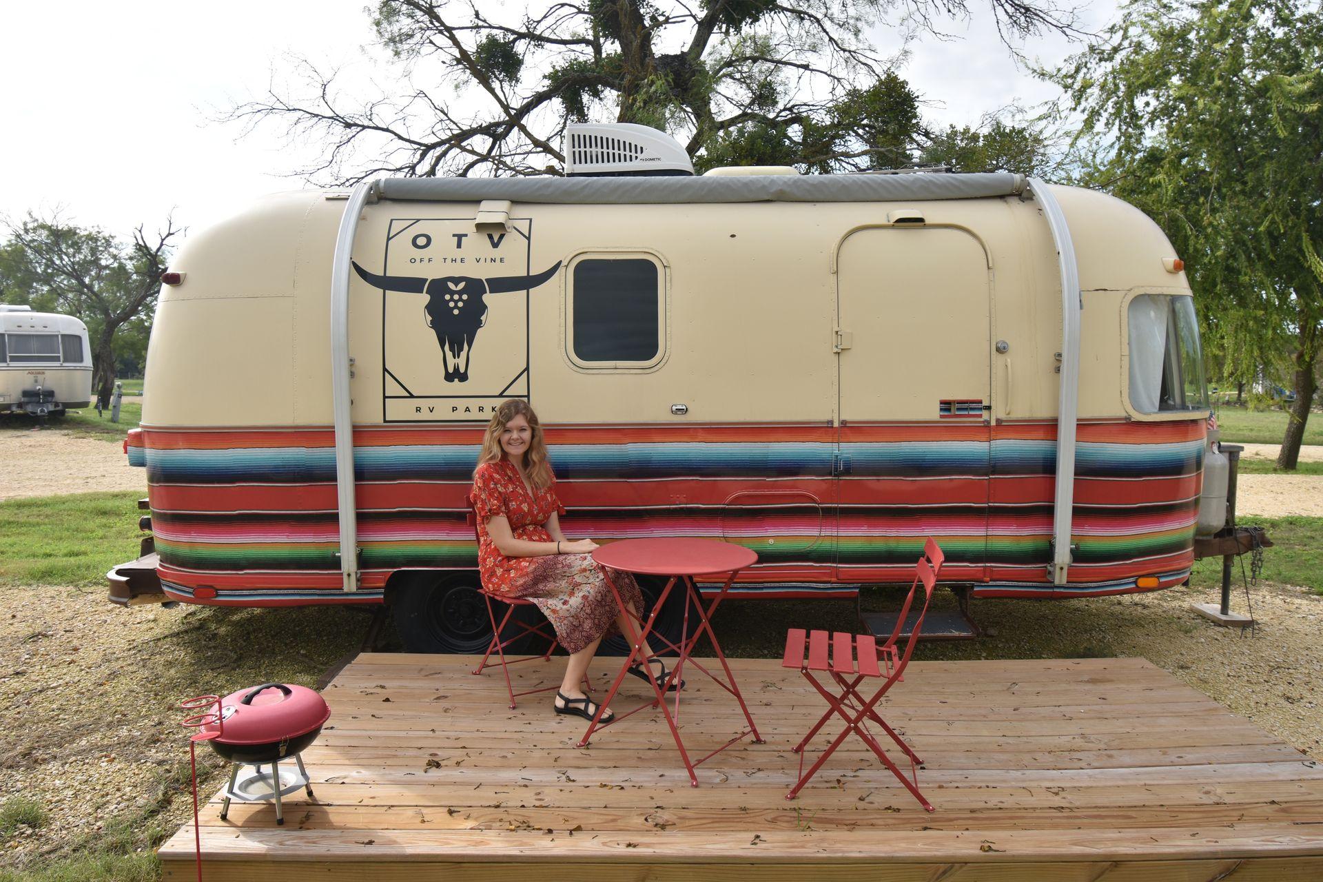 Lydia sitting in front of a colorful trailer that has colorful stripes inspired by a sombrero.