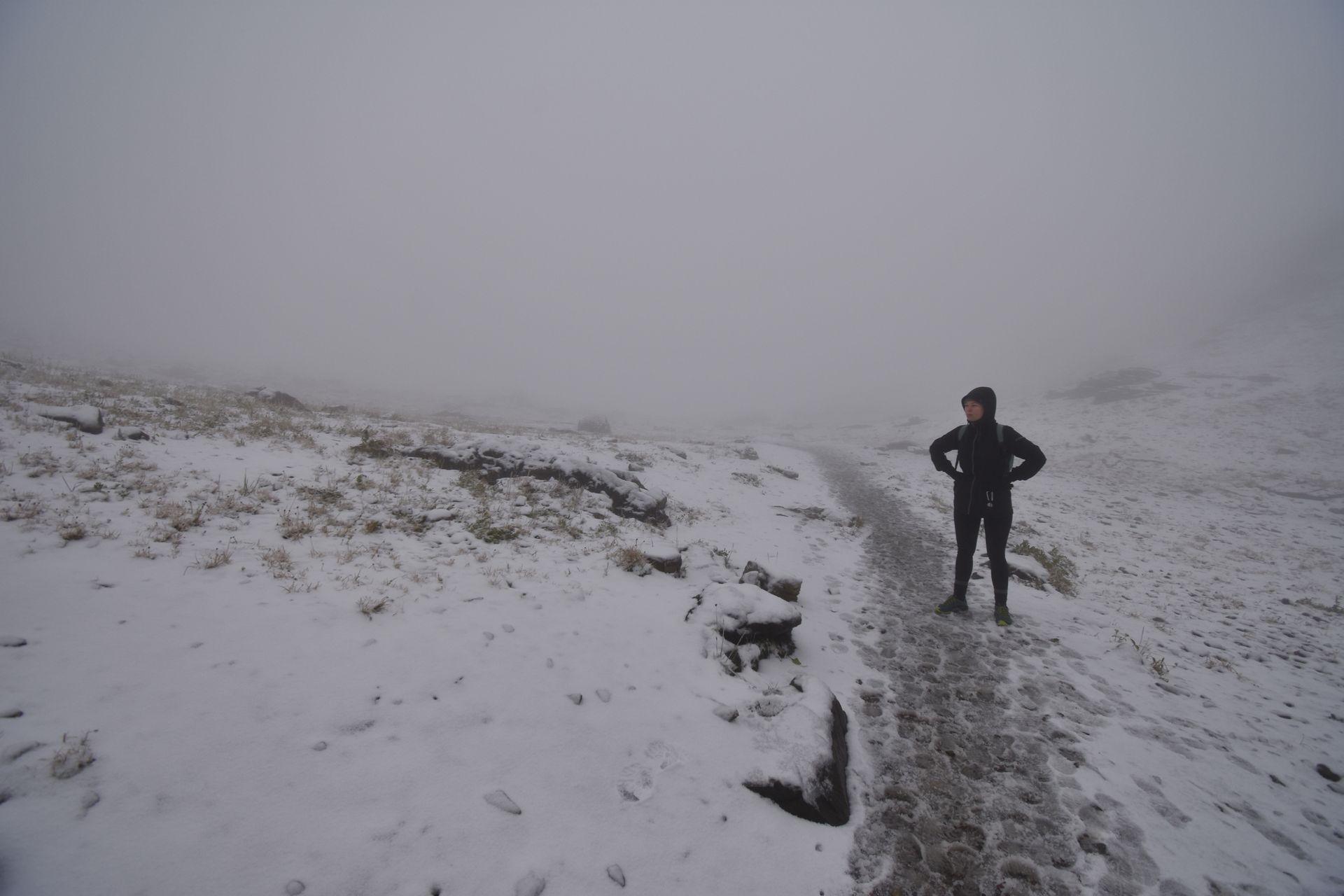 Someone surrounded by fog, standing on a trail covered with snow.