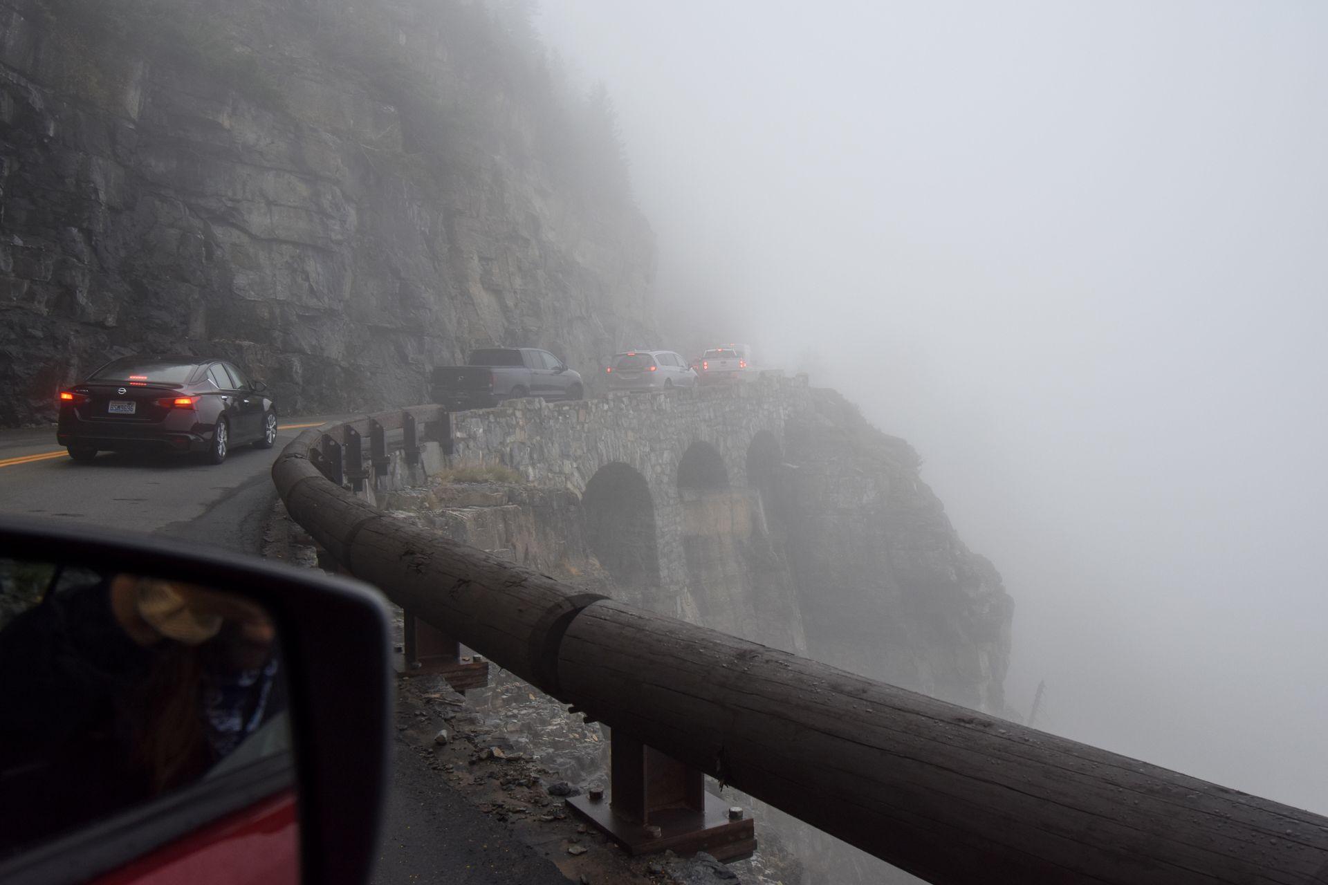 A line of cars on the Going-to-the-Sun road driving through thick fog.