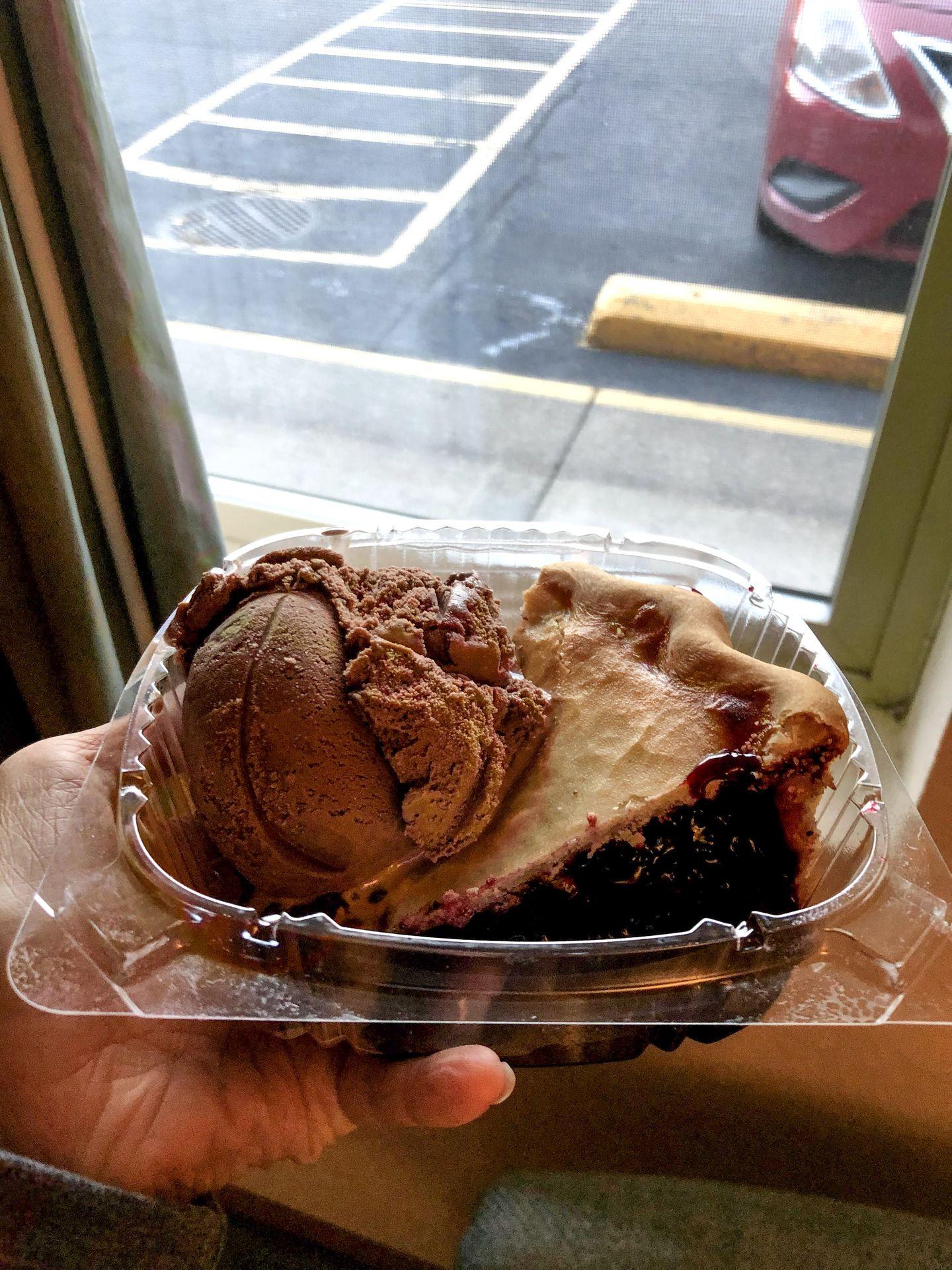 Holding up a plastic container with a slice of pie and a scoop of chocolate ice cream.