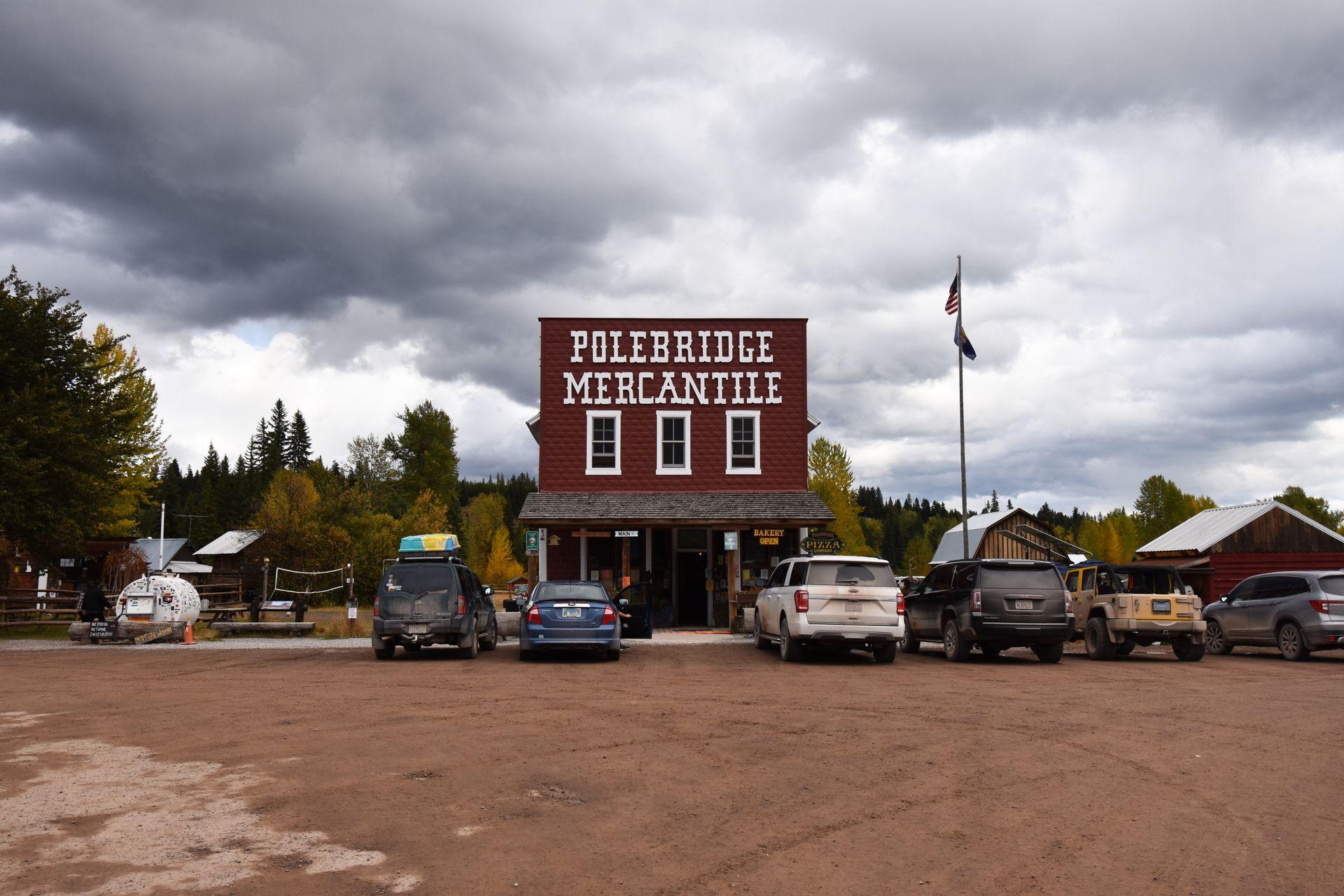 A red brick building with the words "Polebridge Mercantile" attached in white. There are several cars parked in front of the small bakery.