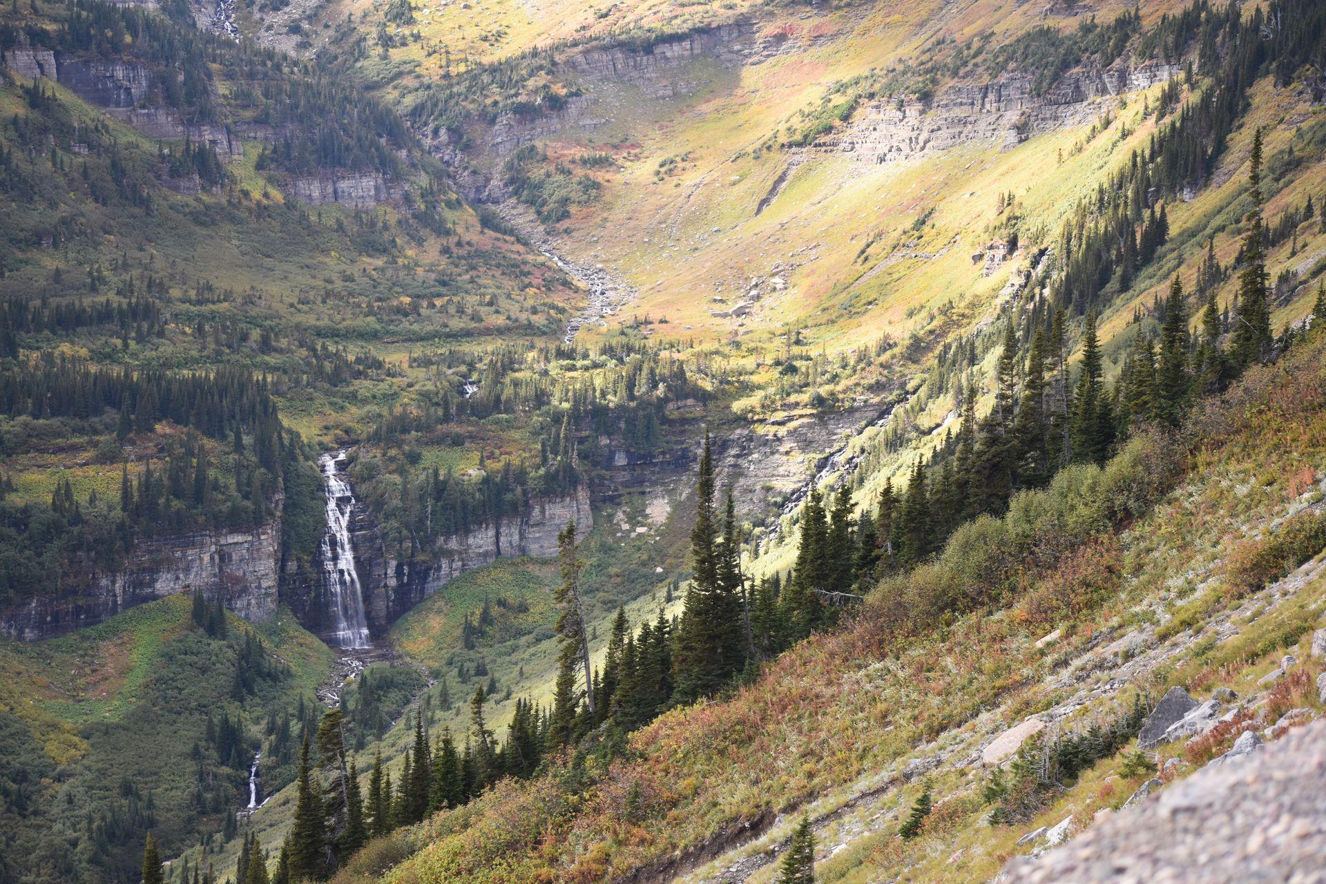 A view of a valley with a waterfall cascading down a cliff. It is a view from the Going-to-the-Sun Road.