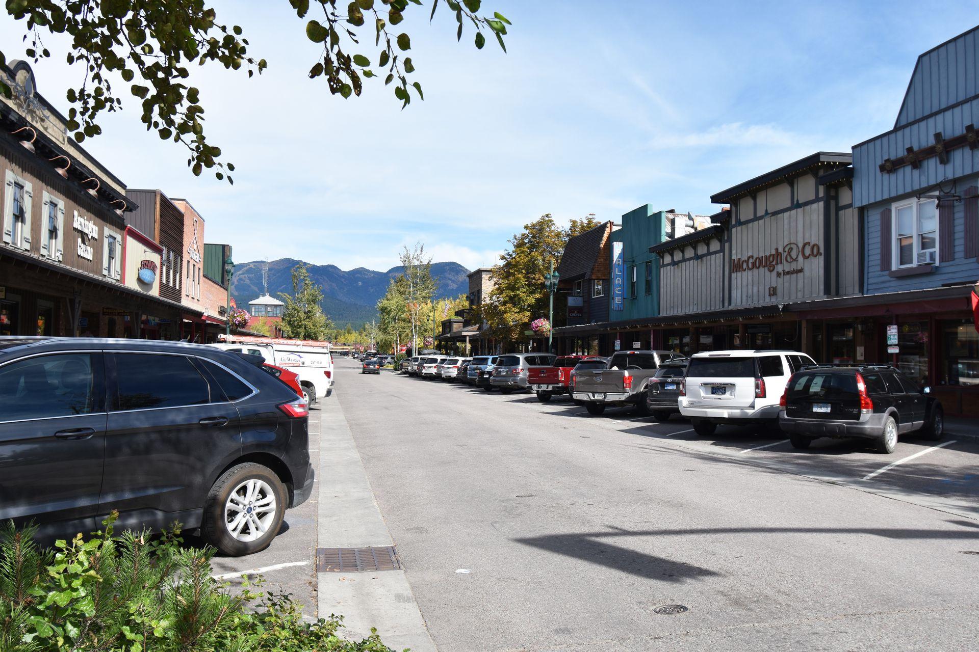 A street in Whitefish. There are shops on both side of the road and cars parking along the street.