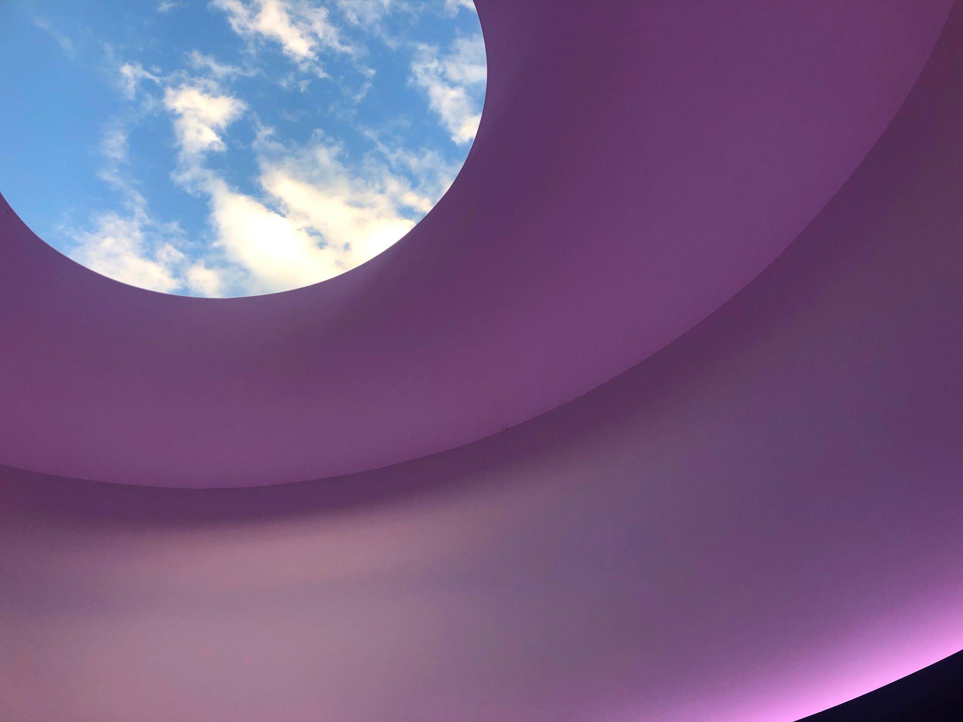 An art installation with purple light and an opening that shows view of the sky