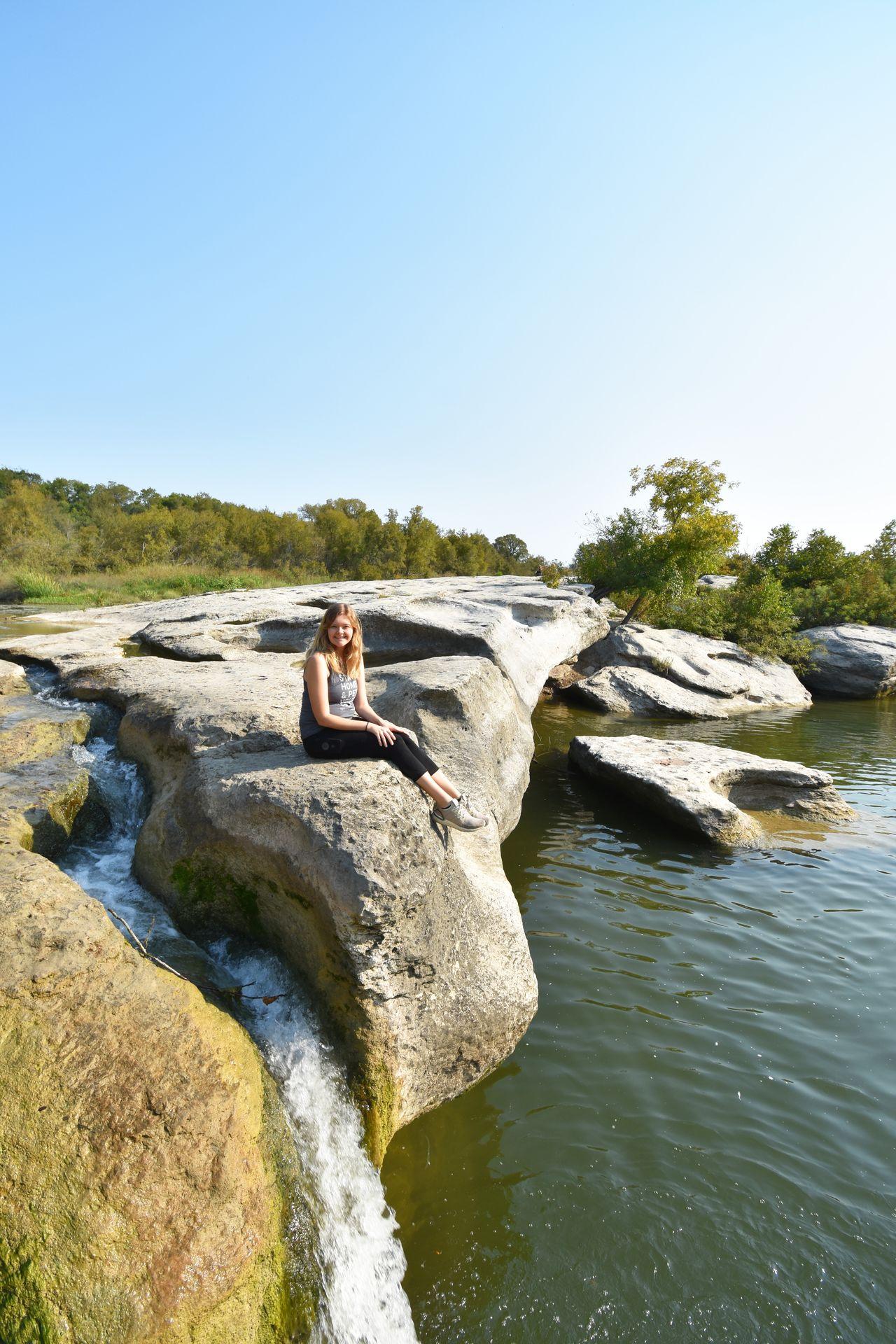 Lydia sitting on a rock at Upper Falls in McKinney Falls State Park