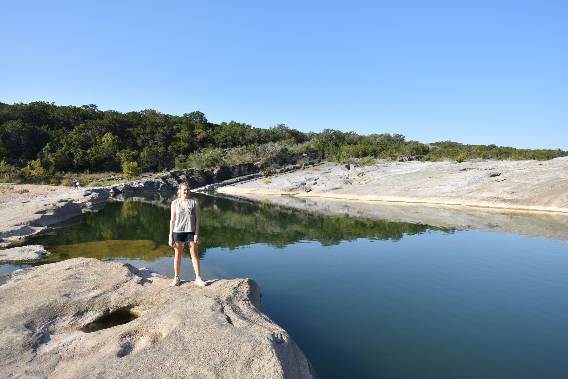 Lydia standing on a rock with water in the background at Pedernales Falls
