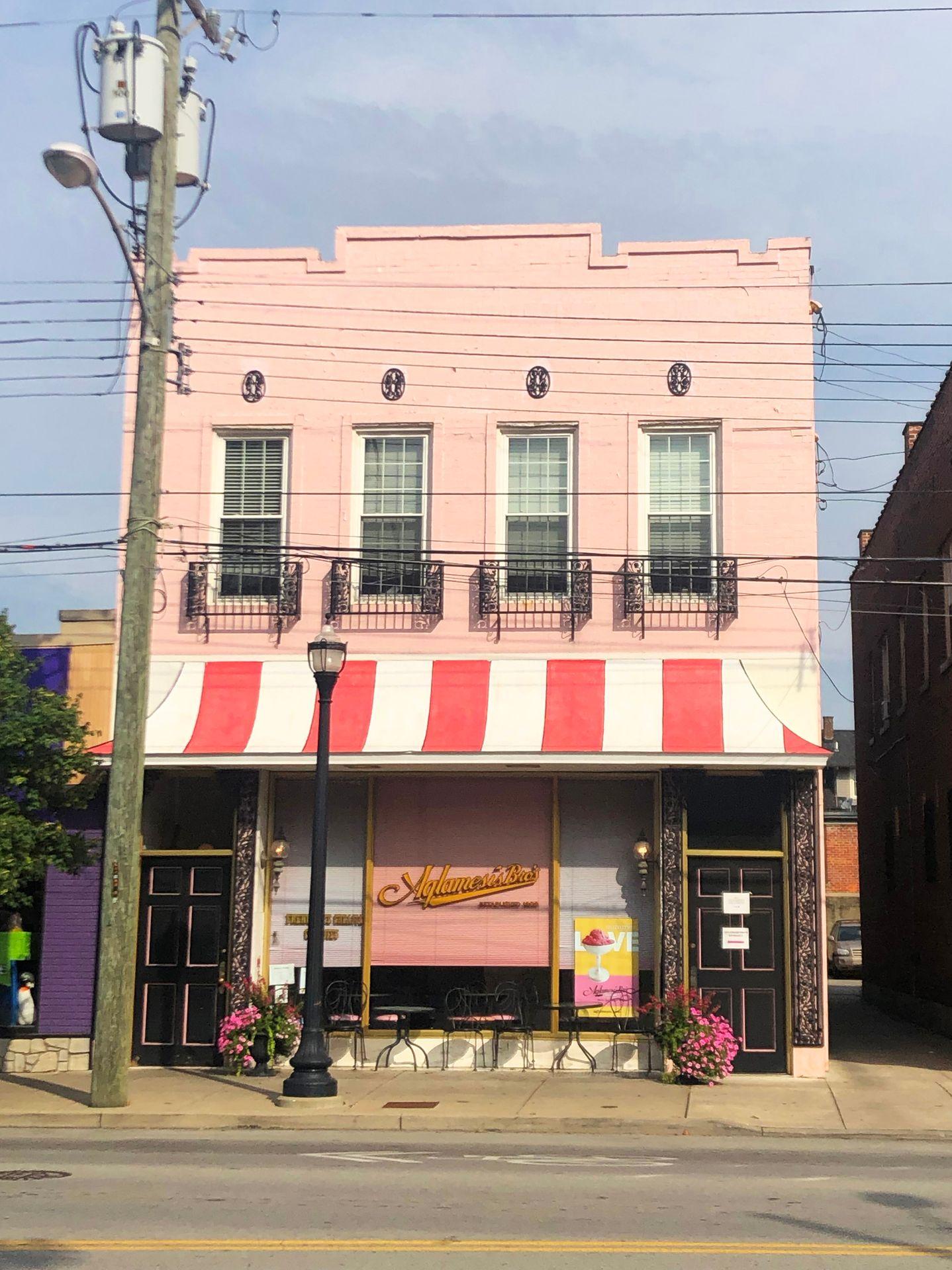 A photo of the Aglamesis Bros exterior. The building is pink with a pink and white striped awning.