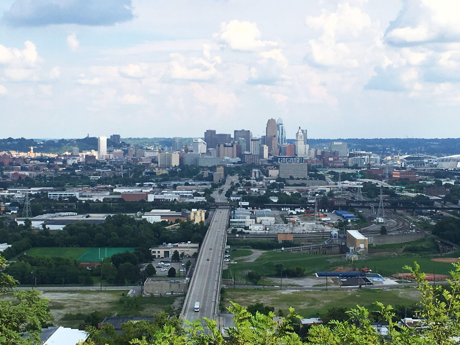 A view of the Cincinnati skyline from Price Hill. There is a highway bridge between the viewer and the city. One building downtown has the word 'Cincinnati' written on it.