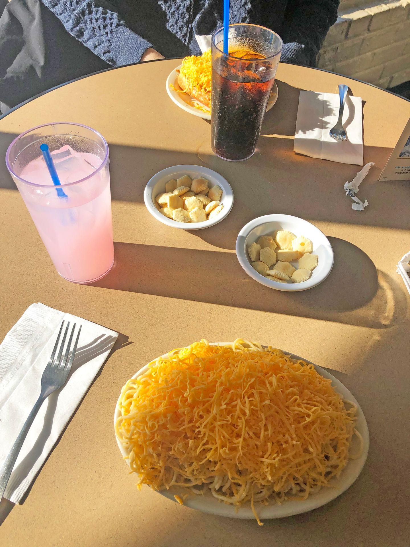 Looking down a plate of spaghetti and cheese with bowls of oyster crackers and a pink lemonade.
